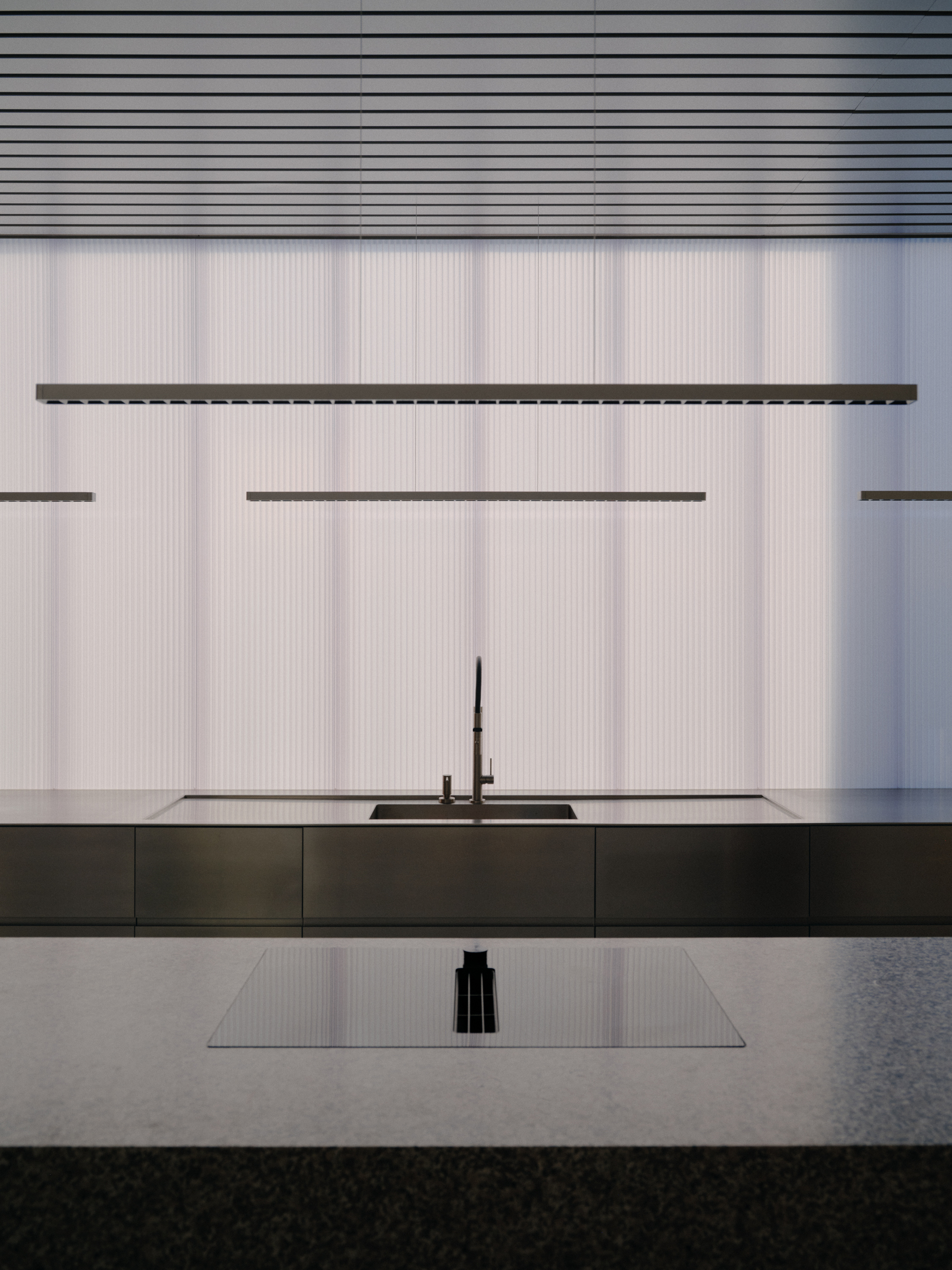Kitchen island with black countertop against white ribbed wall and linear suspension lights