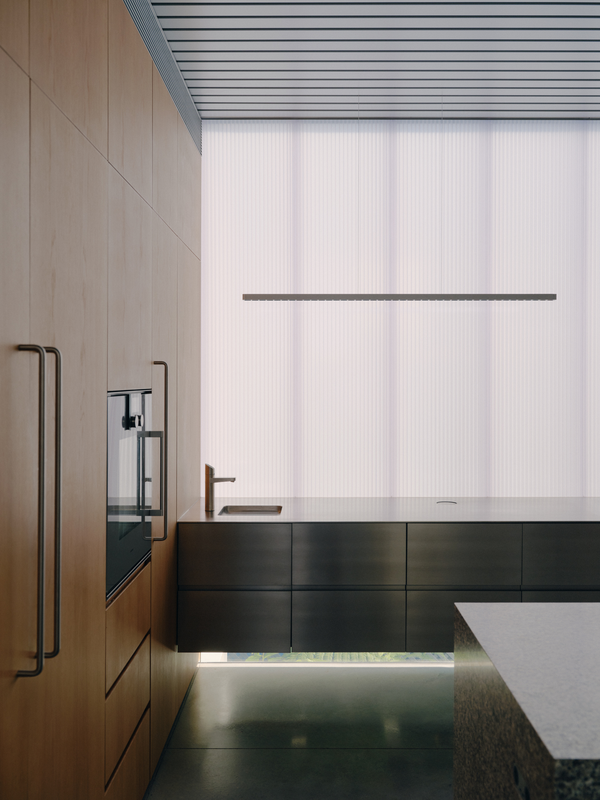 Kitchen with timber cabinetry, black base units, and translucent corrugated wall panels in soft daylight