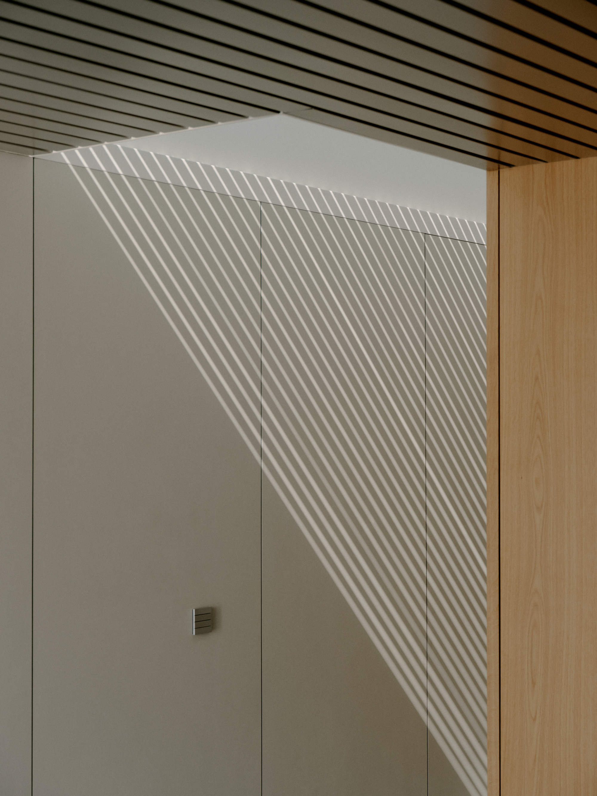 White wall with linear shadow pattern from slatted ceiling illumination falling across doorway