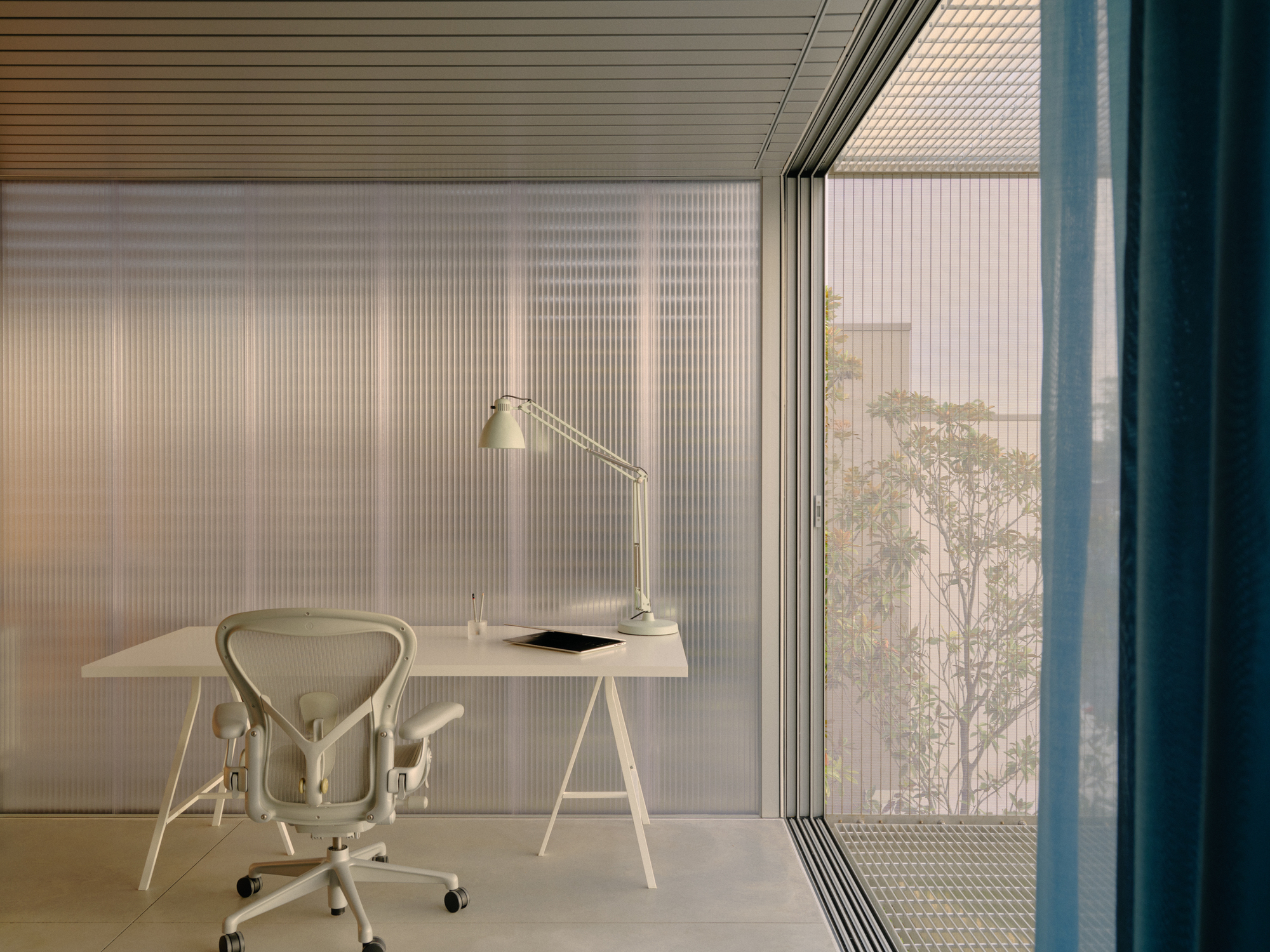 Home office with trestle desk and fluted glass wall opening to balcony at dusk