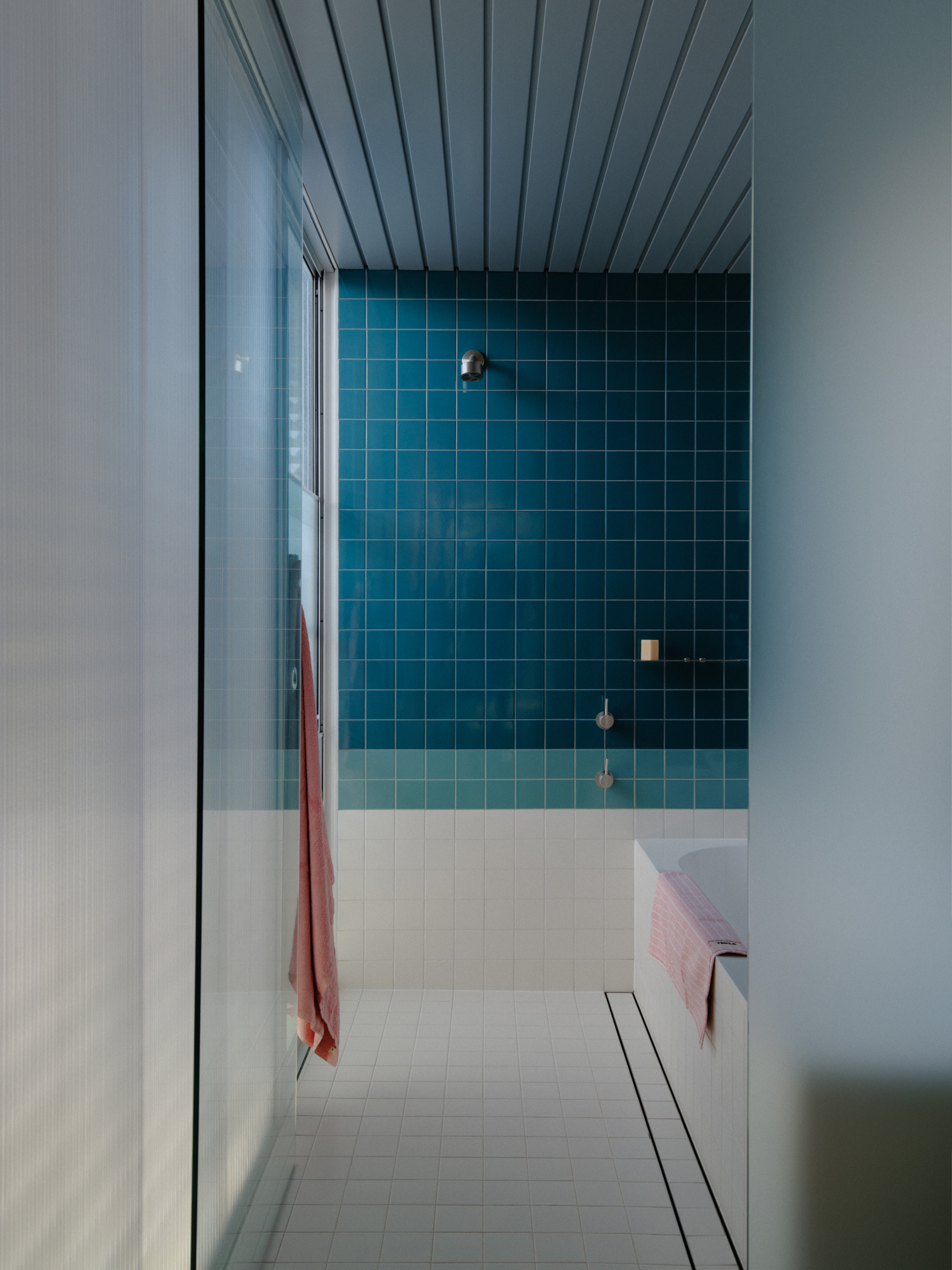 Bathroom doorway view showing teal tiled shower enclosure and white floor tiles