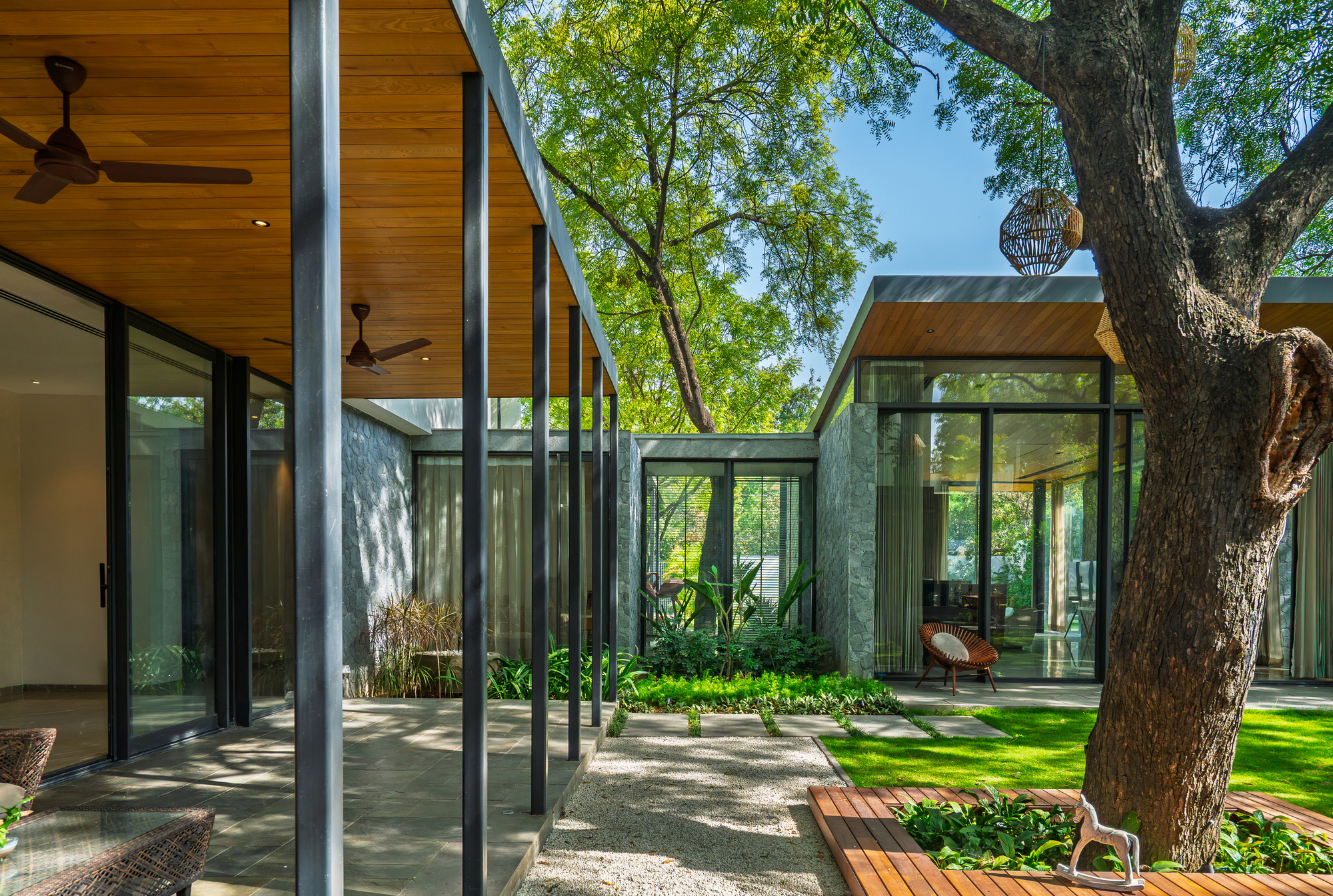Multiple glass-walled pavilions with timber soffits arranged around a central garden with mature trees