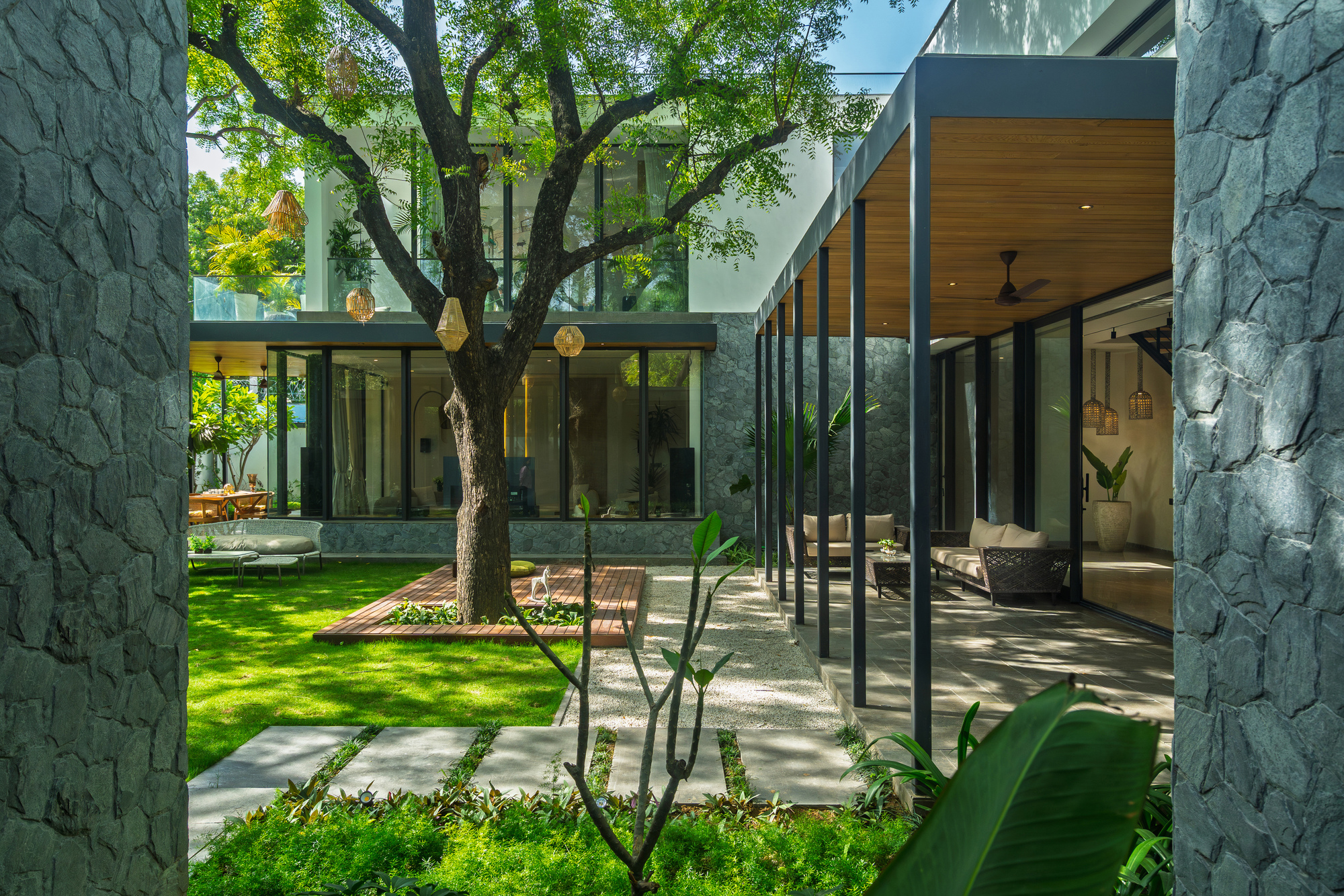 Courtyard with stone-clad volumes, glazed walkways, and an existing tree preserved in the lawn
