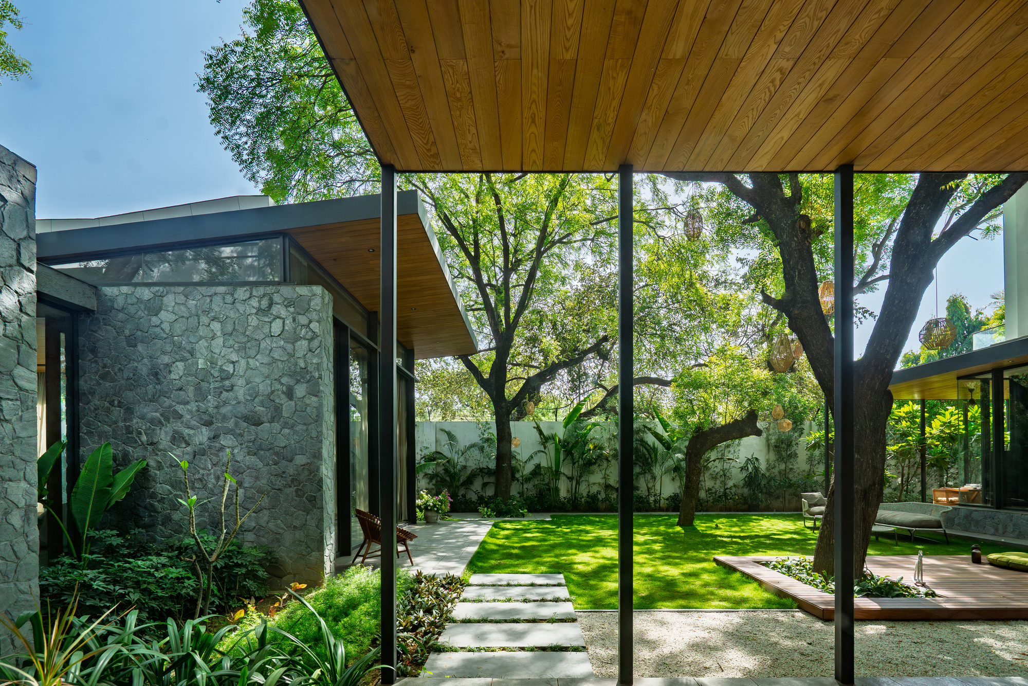Covered passage with timber soffit and steel columns framing views of the garden and stone walls
