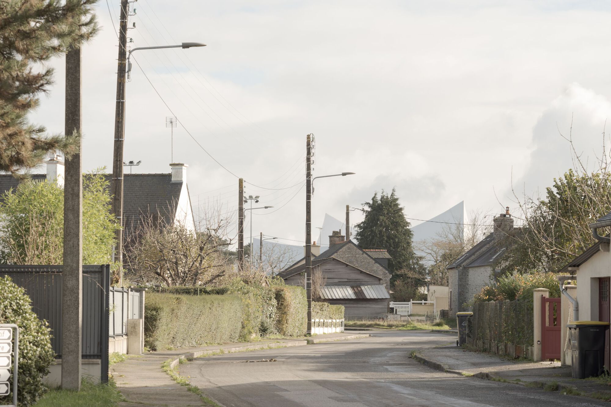 Village street with utility poles and houses leading toward the white peaked roof in the distance