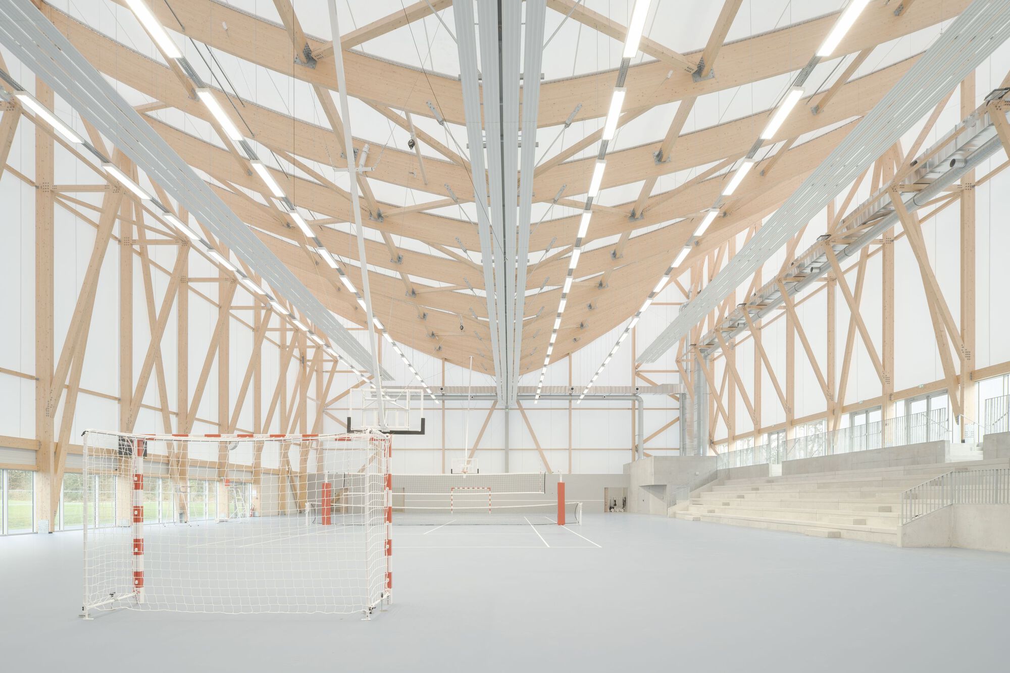 Interior sports hall with exposed timber truss roof structure and bleacher seating