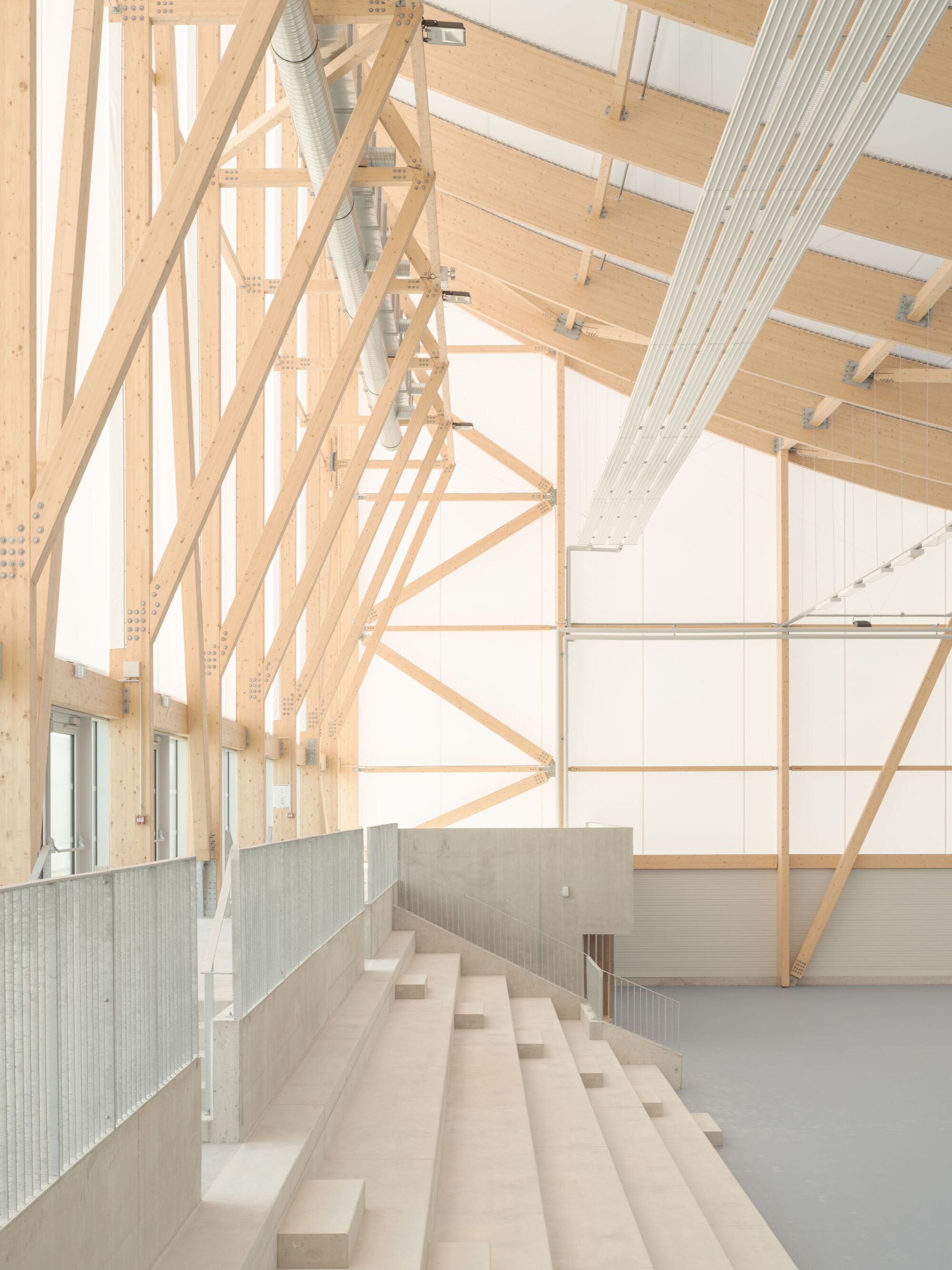 Concrete bleachers under diagonal timber roof trusses with corrugated metal balustrade