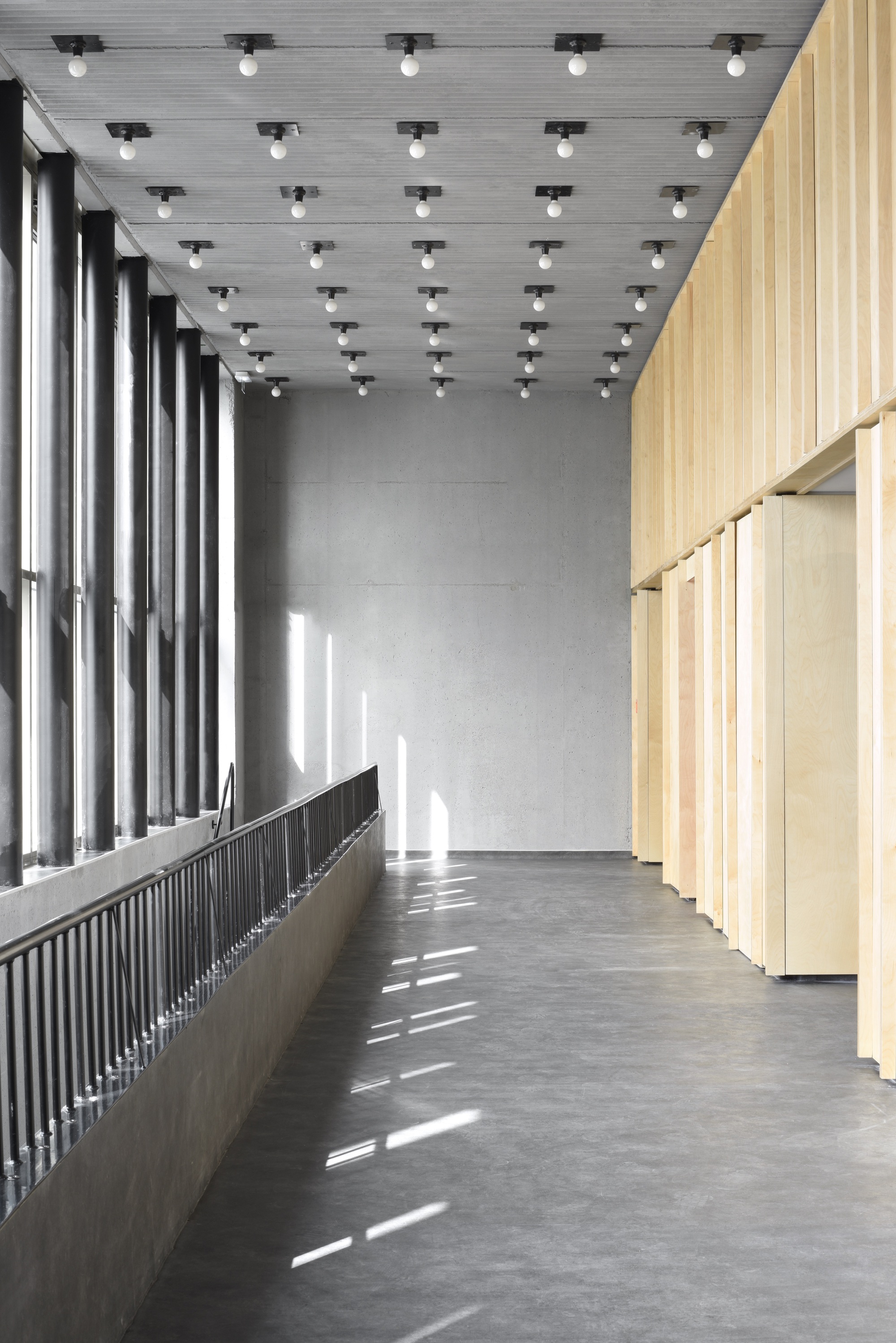 Interior corridor with vertical black radiator beneath tall windows casting slanted sunlight on concrete floor