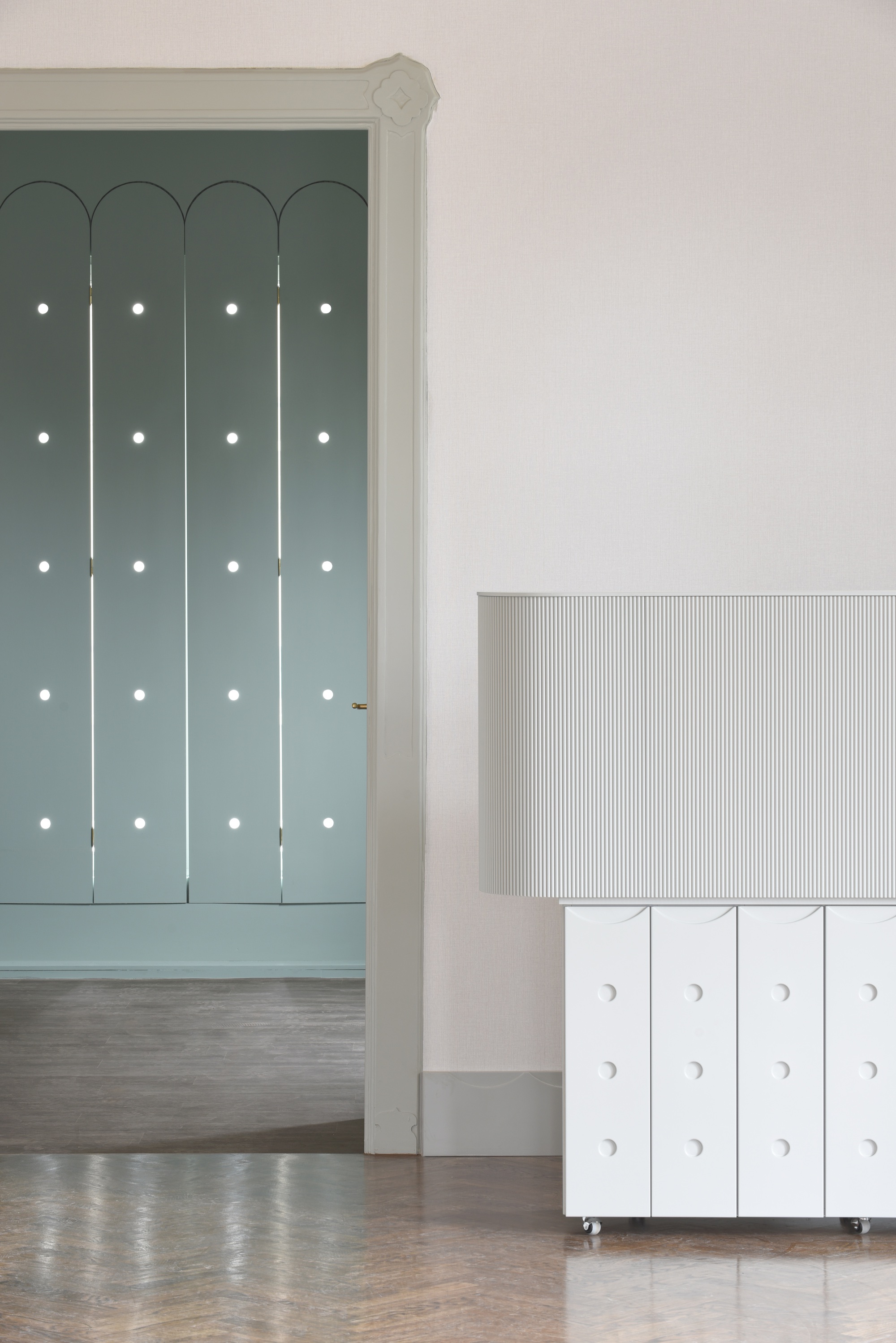 Arched doorway with green panels and white circular pulls beside a wheeled cabinet with ribbed front