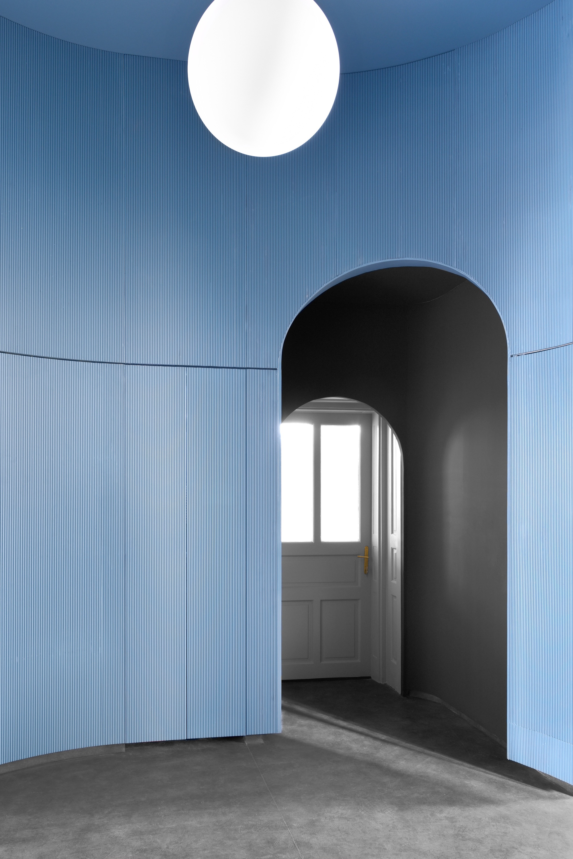 Blue paneled room with black arched portal leading to a white door and hanging globe light