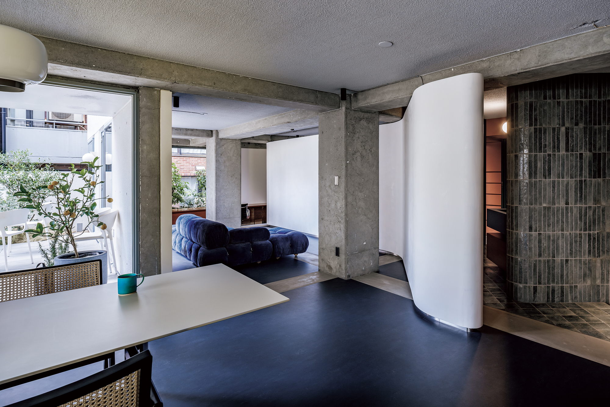 Open living area with exposed concrete beams and curved white partition separating spaces with terrace beyond