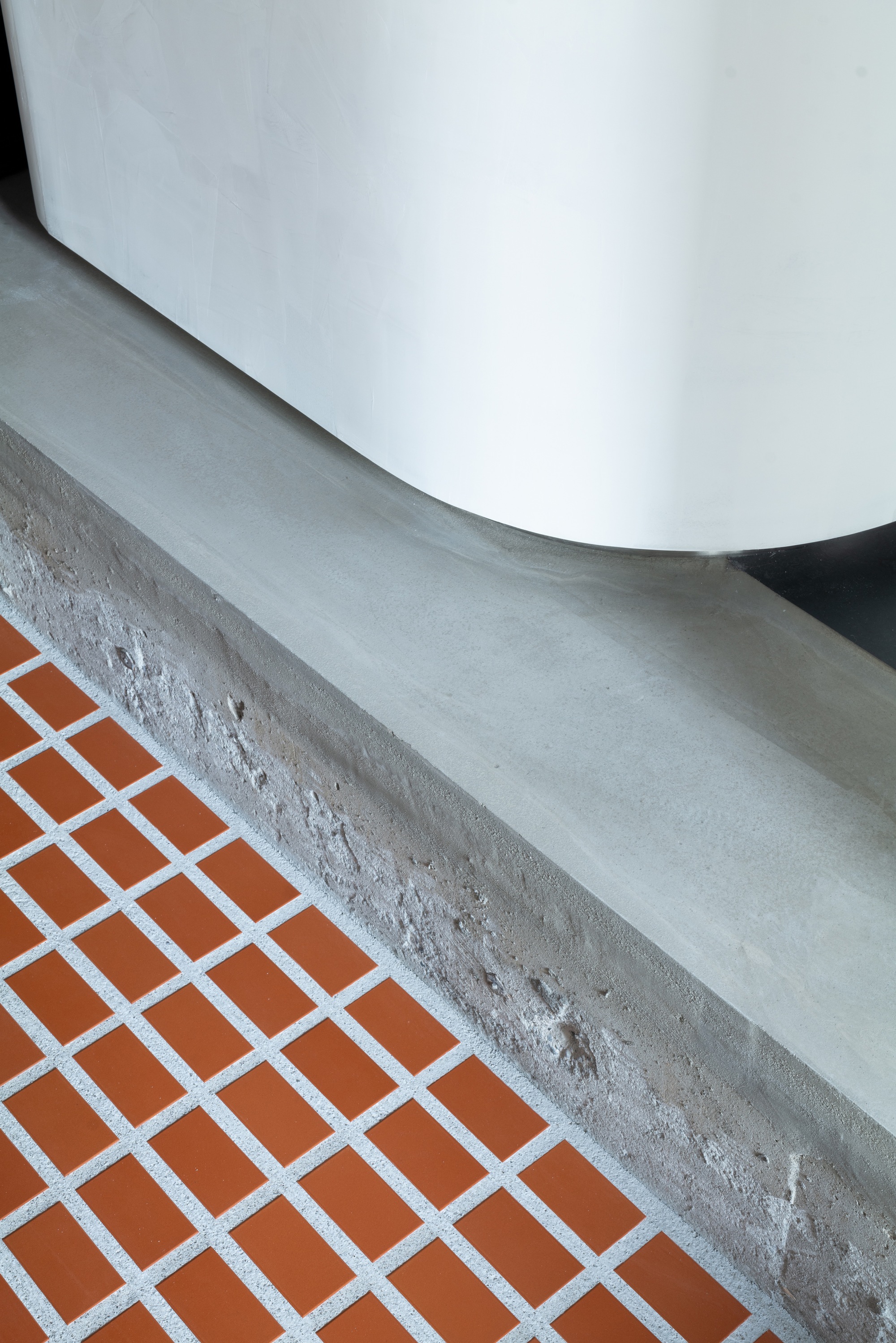Detail of cast concrete ledge meeting white curved wall above orange tile floor with white grout