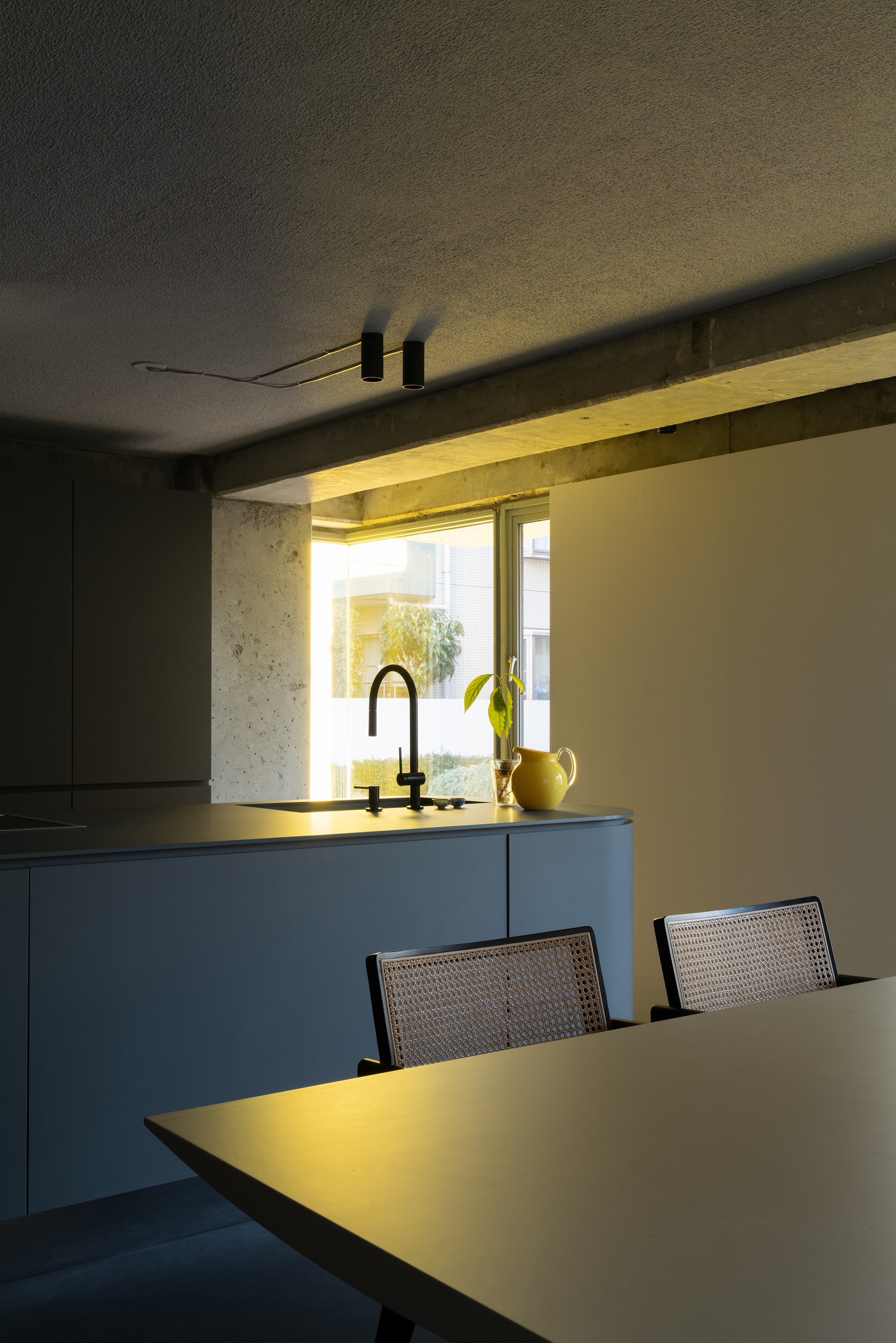 Concrete window niche with integrated yellow lighting framing kitchen sink and yellow pitcher at dusk