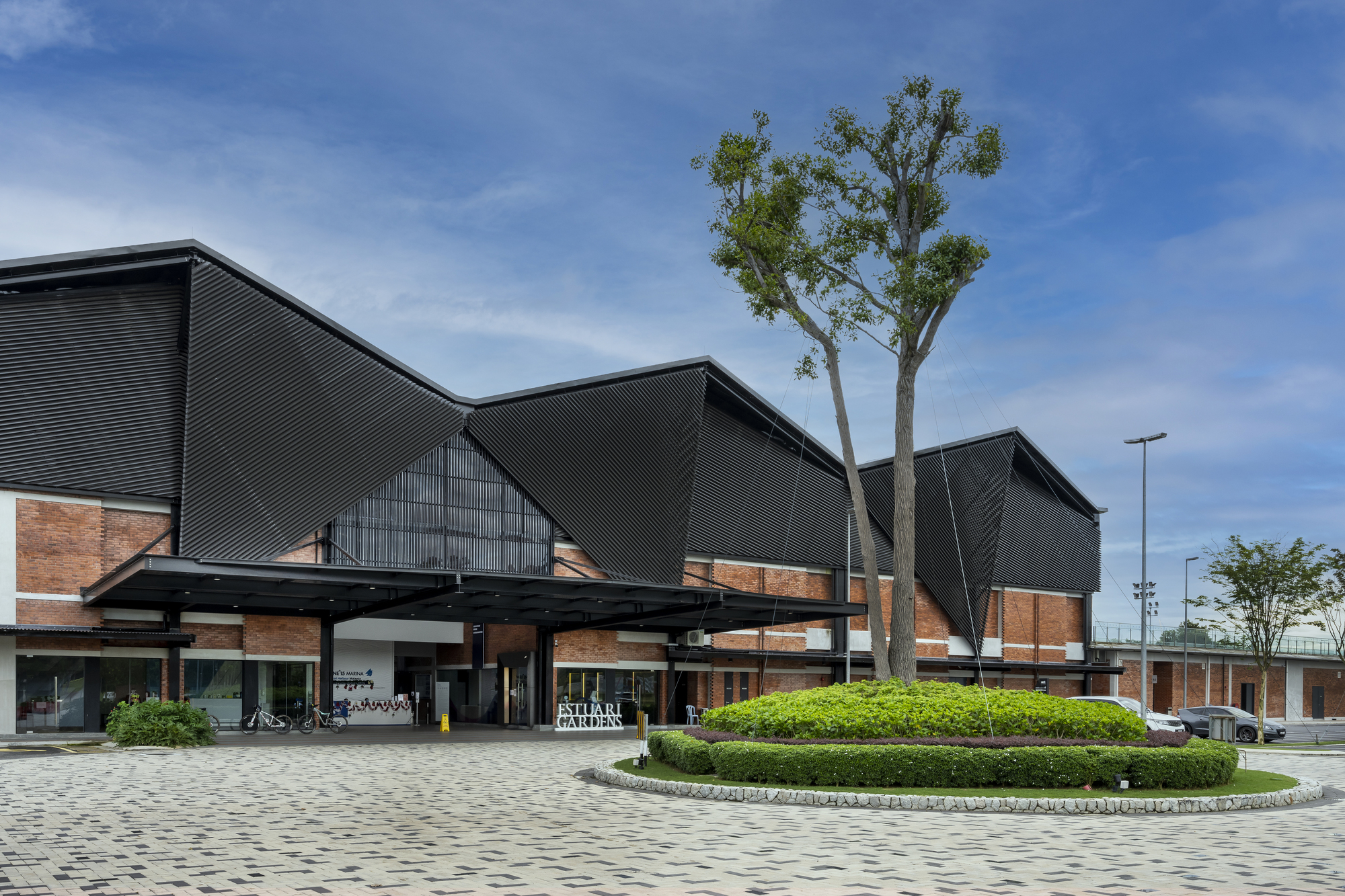Front plaza with brick base, corrugated metal gable roofs, and a single tree under blue sky