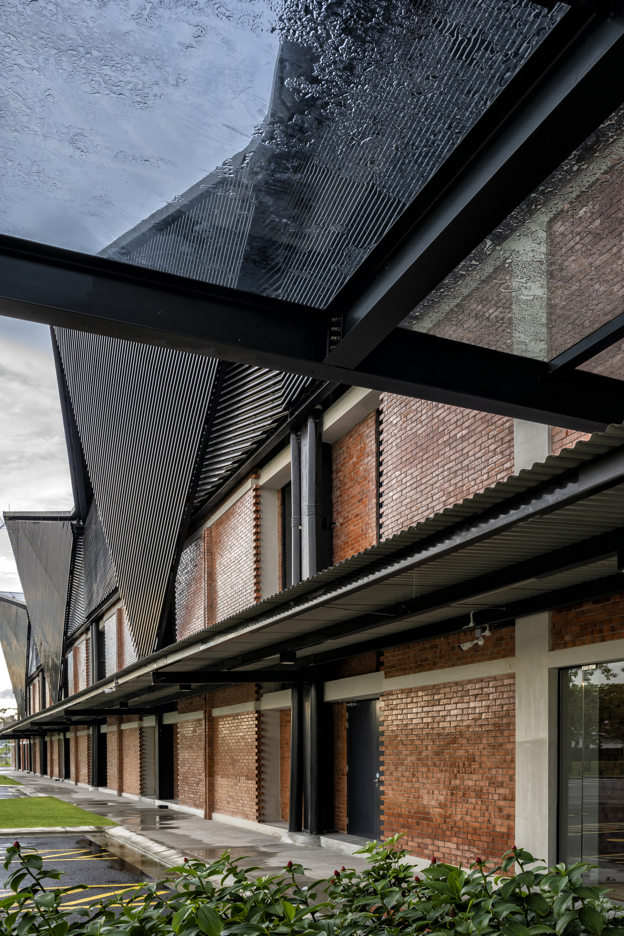 Covered walkway with black steel beams, corrugated metal canopy, and brick facade along glass storefronts