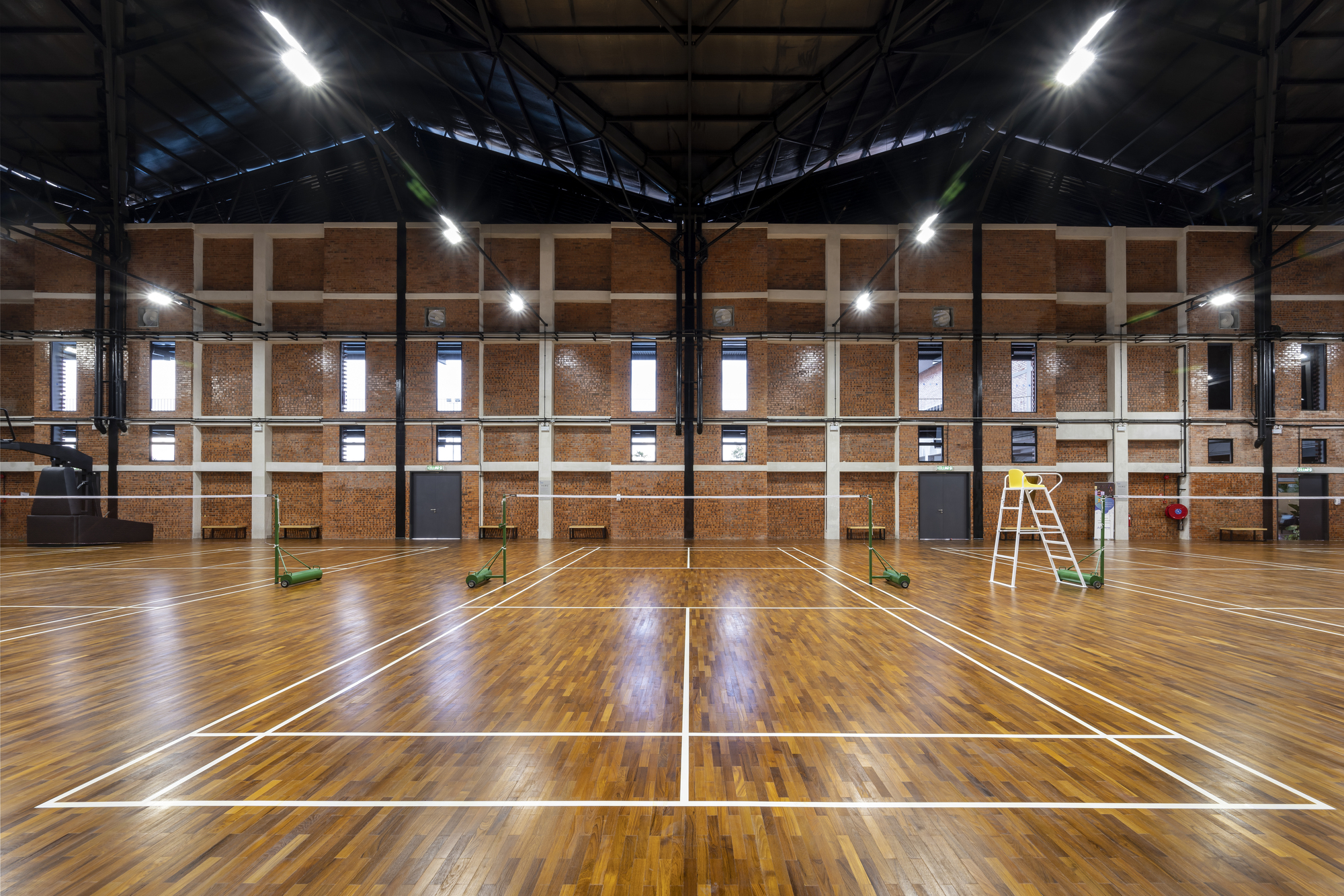 Indoor sports hall with timber floor, exposed steel roof trusses, and brick perimeter walls at night
