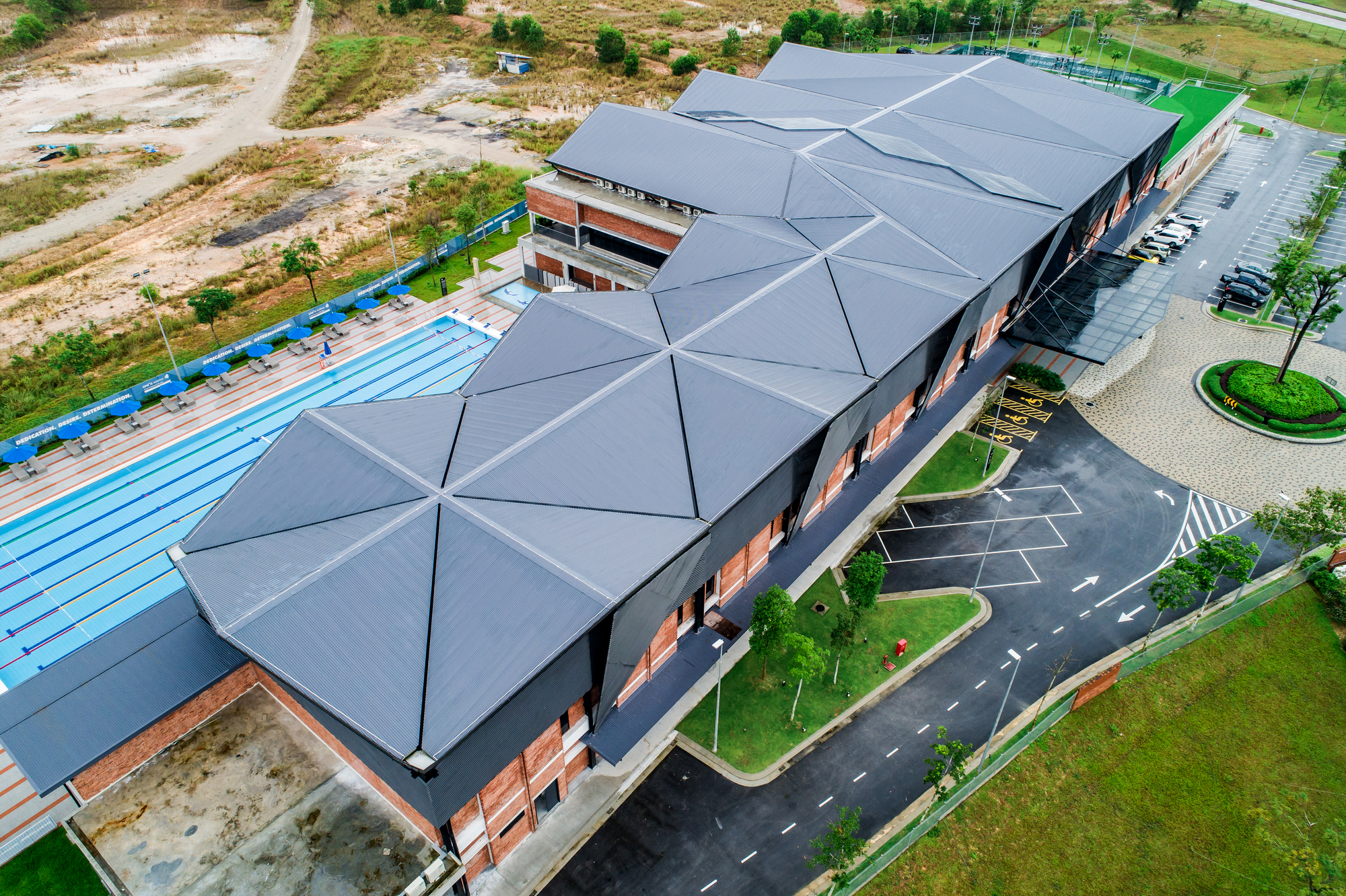 Aerial view of the faceted metal roof form adjacent to a swimming pool and parking area