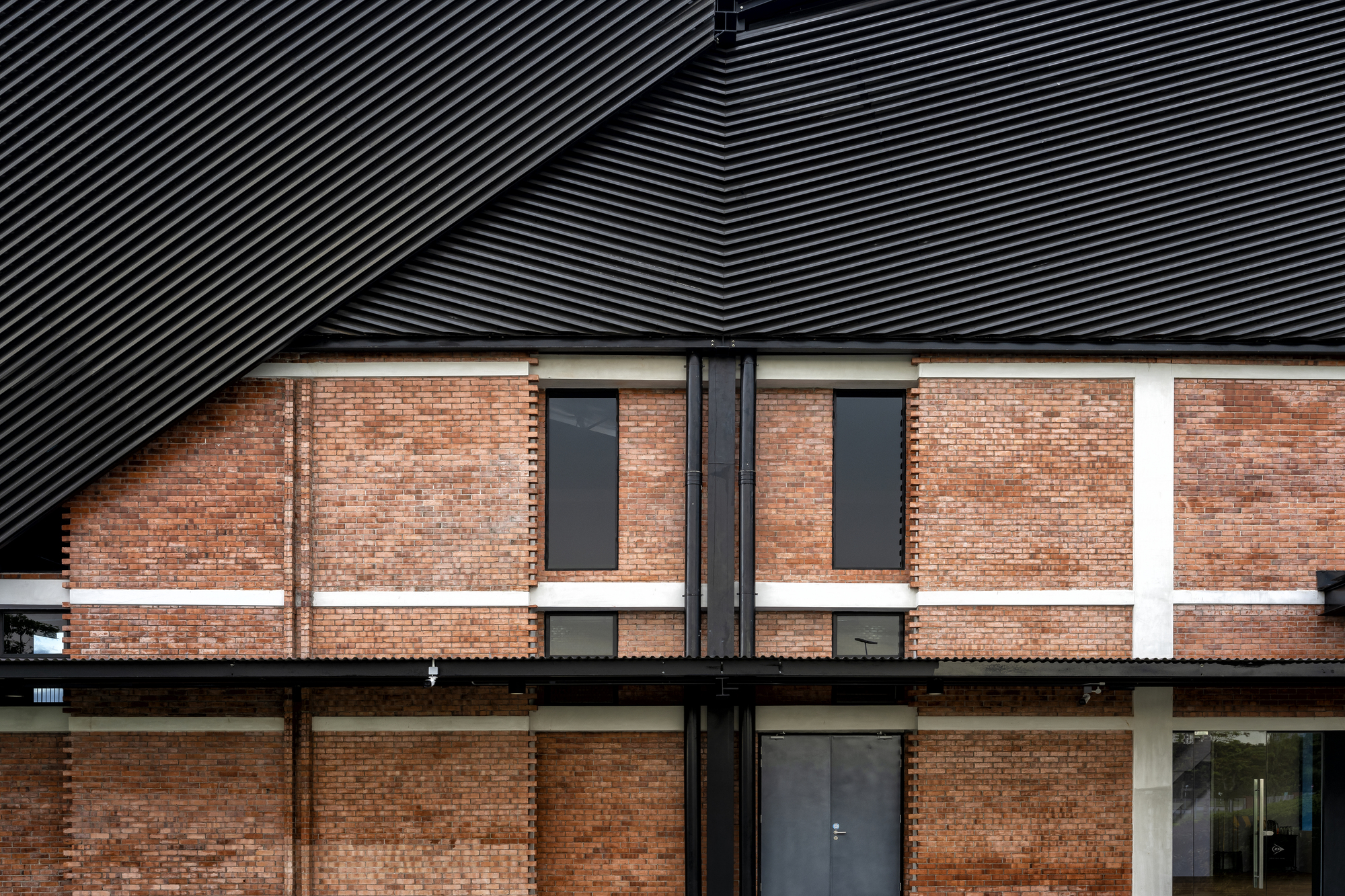 Facade detail showing brick walls with horizontal banding beneath ribbed metal roof planes