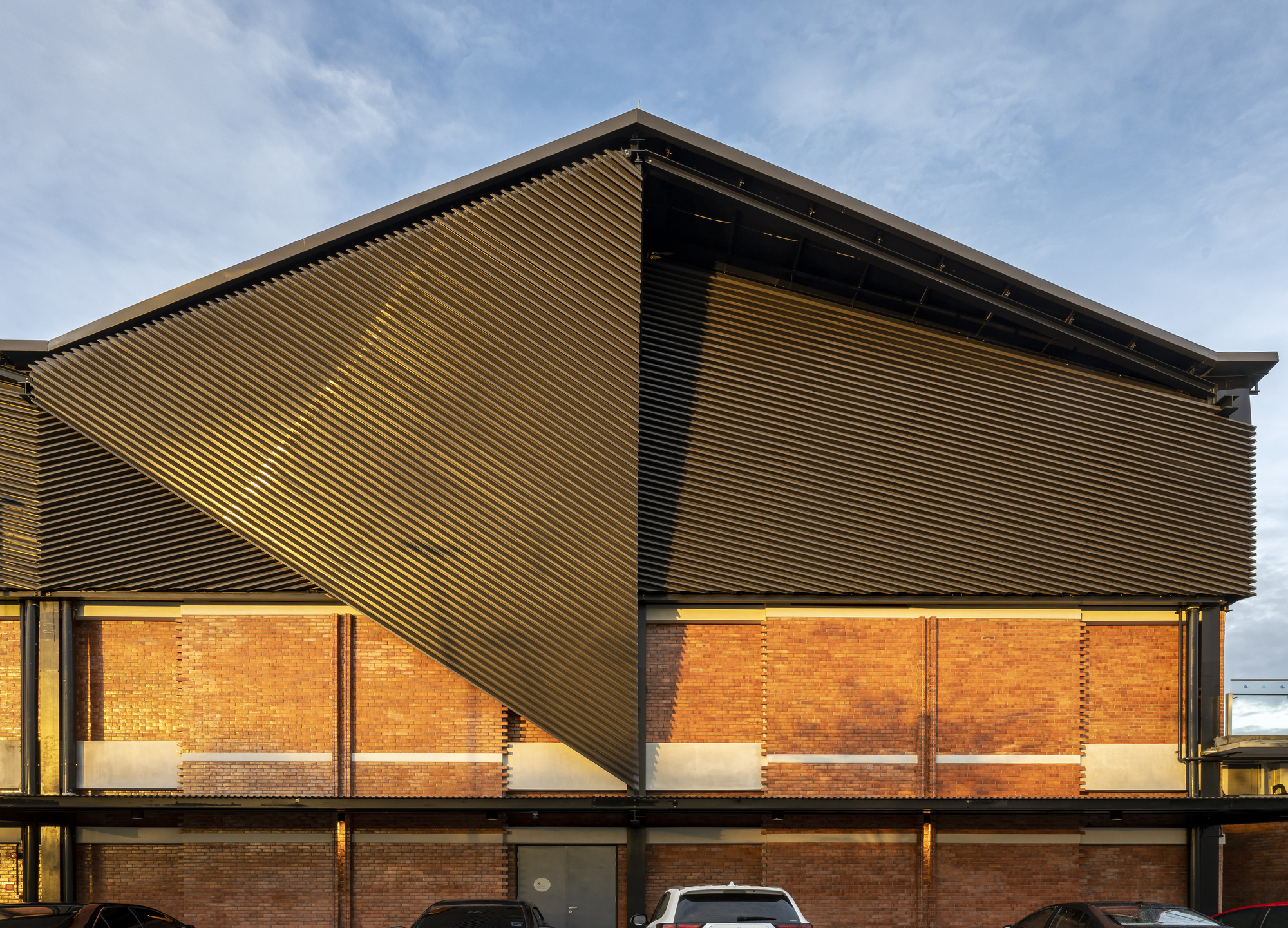 Corrugated metal cladding wrapping the upper volume above a brick facade at dusk