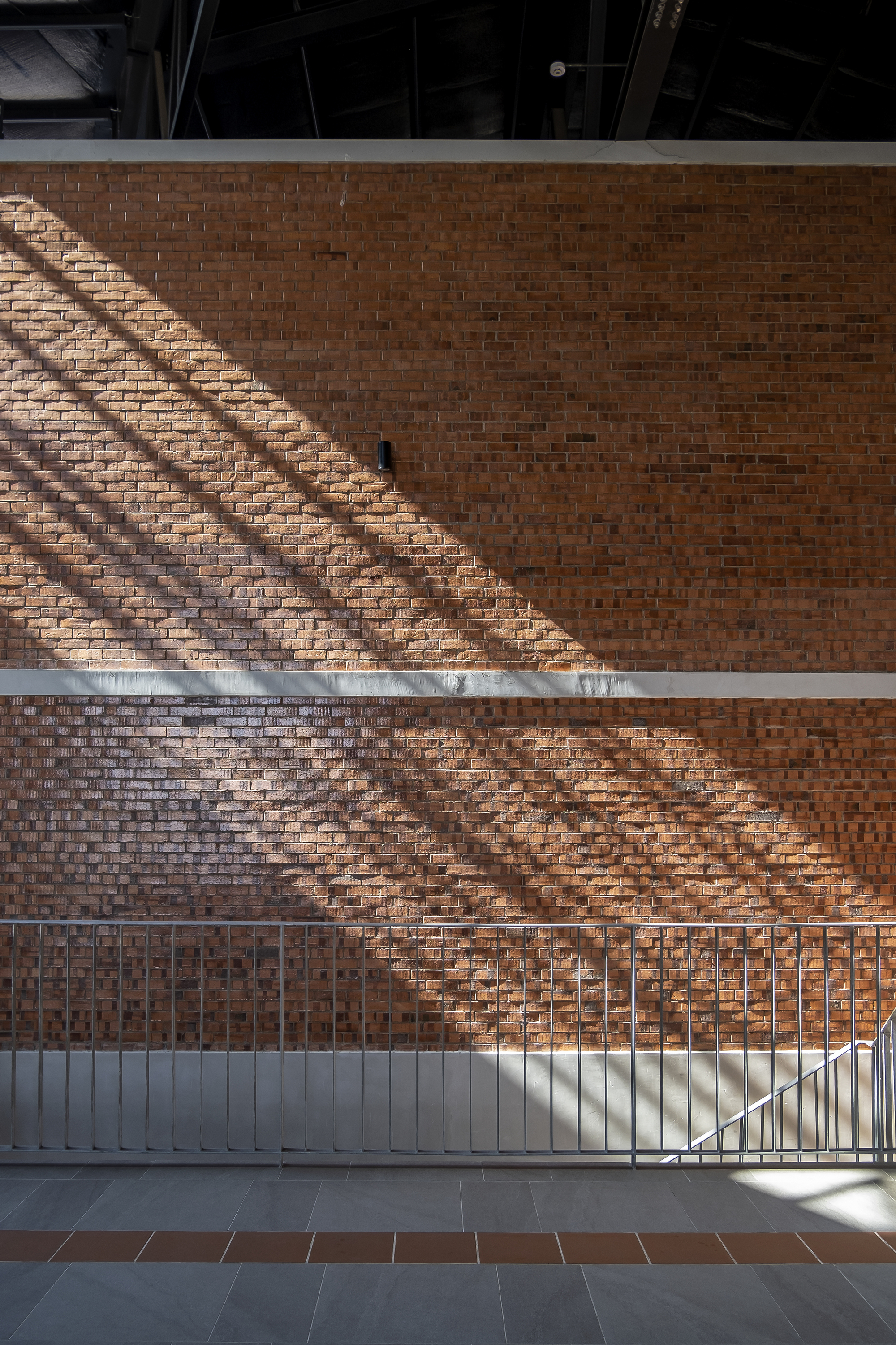 Perforated brick wall with diagonal shadow patterns cast from structural elements above