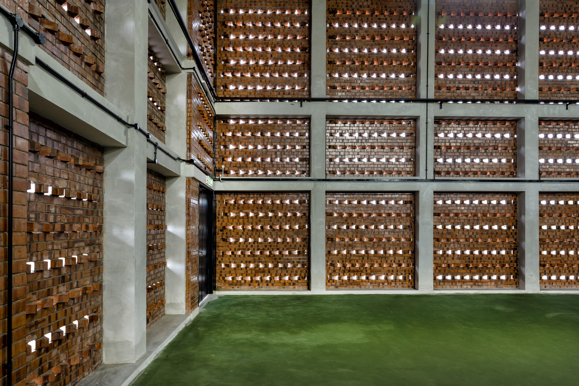 Perforated brick screen wall with concrete frame grid and green turf floor below