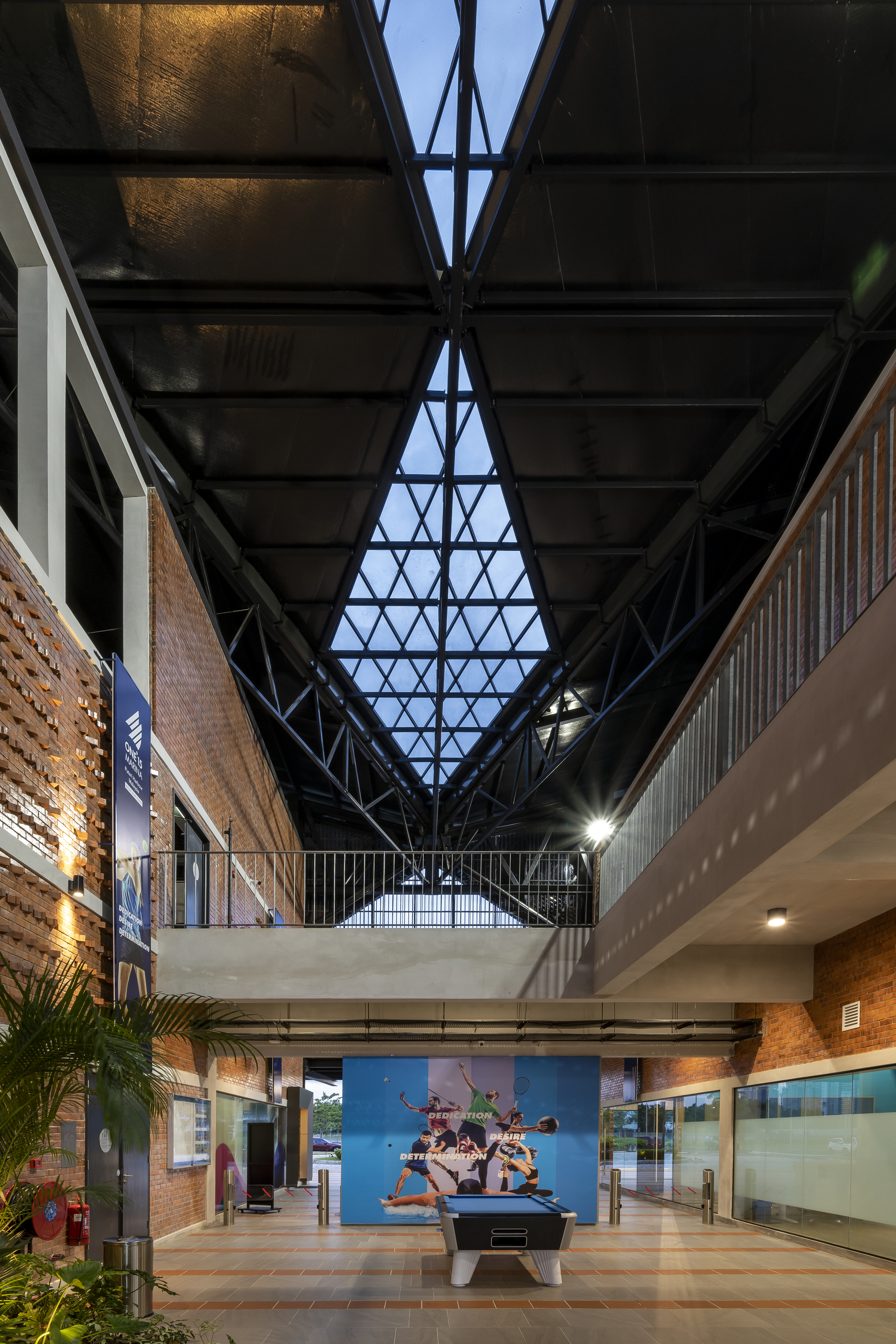 Central atrium with triangular skylight framed by black steel trusses at dusk
