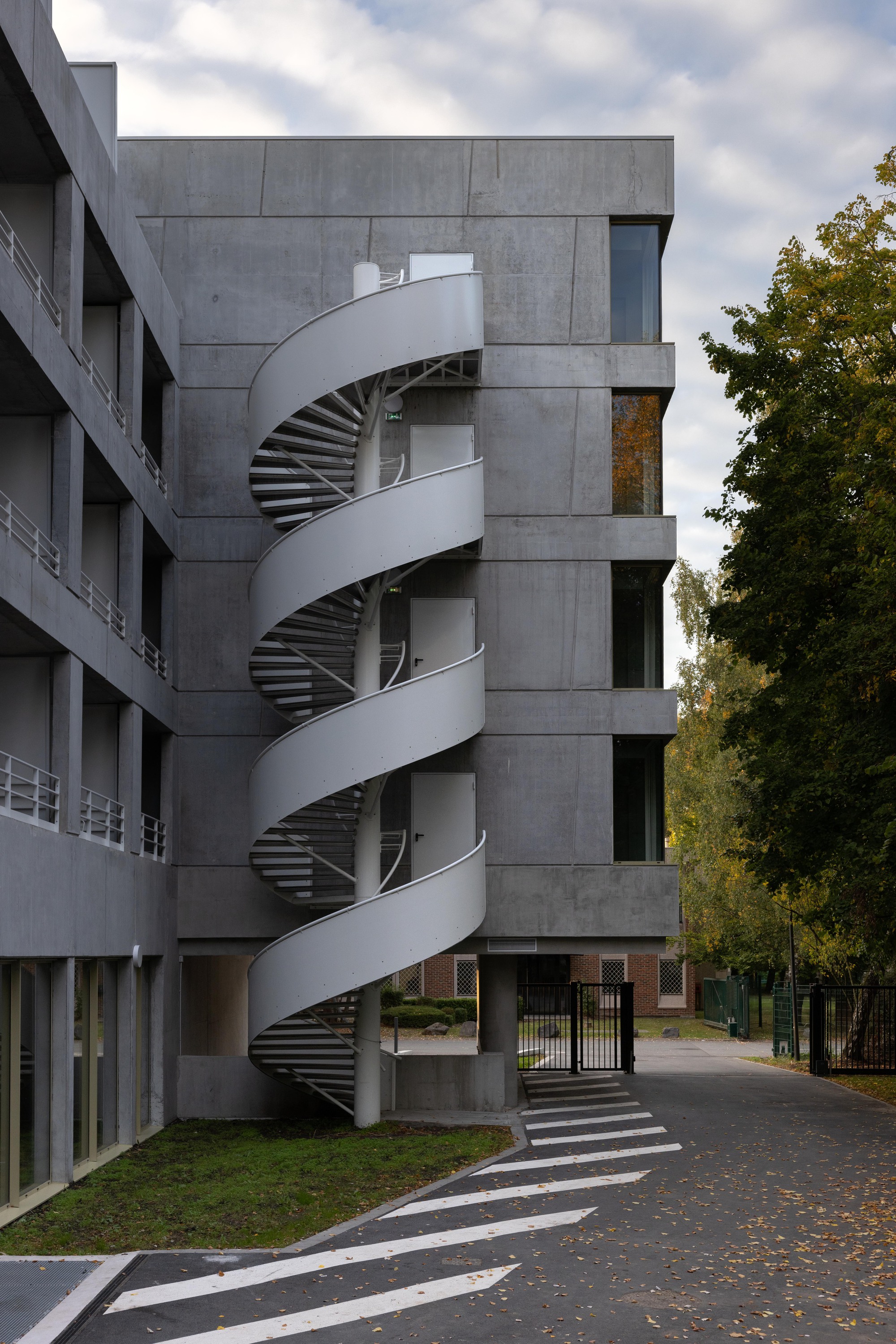 White helical exterior staircase wrapping around concrete tower beside a road with fallen autumn leaves
