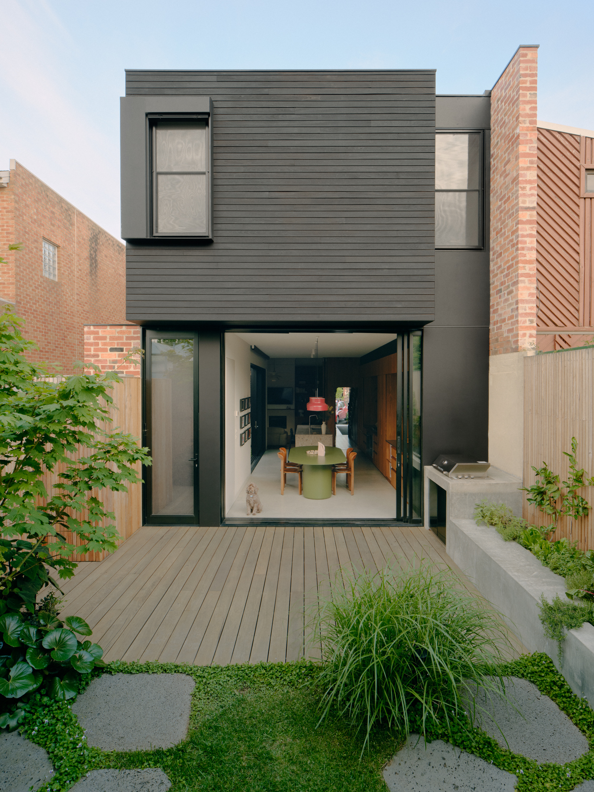 Rear courtyard garden with timber decking leading to large sliding glass doors at dusk