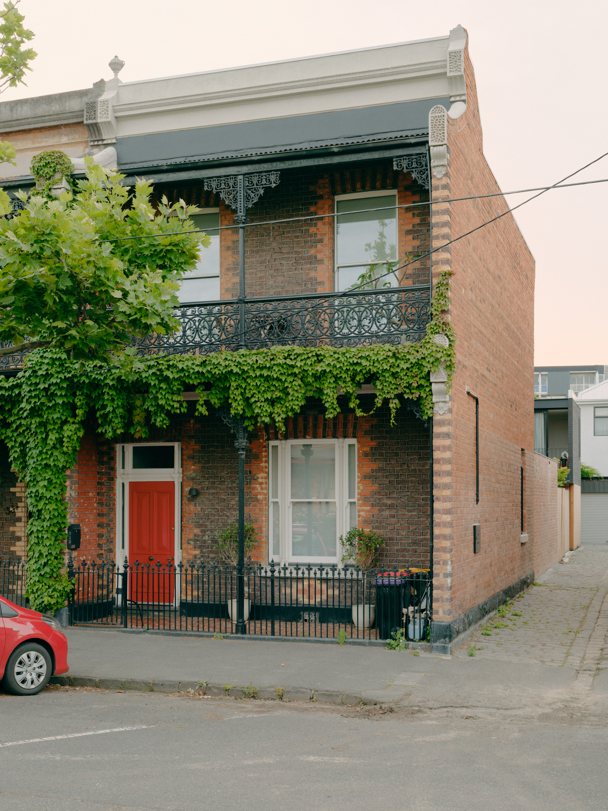 Historic terrace house with ornamental ironwork balcony and ivy-clad facade beside newer brick extension