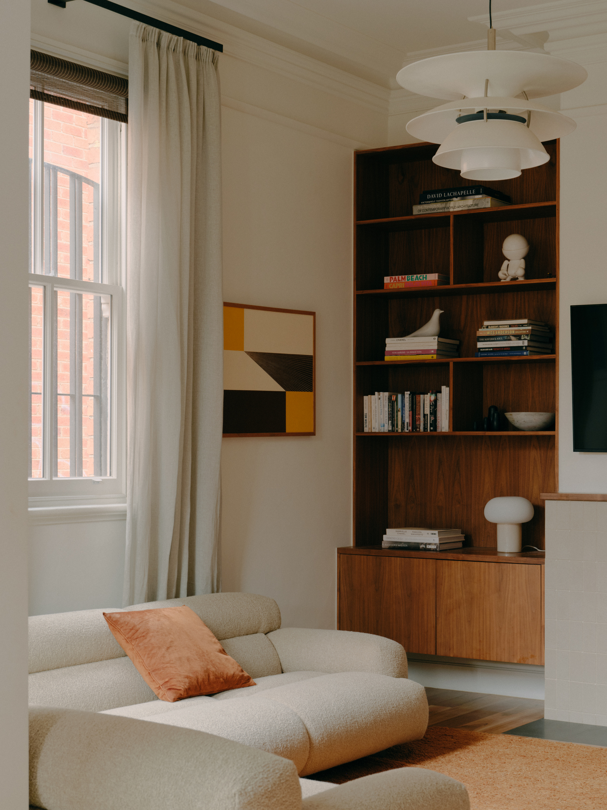 Living room with tall walnut shelving unit and tiered pendant light fixture above sectional seating