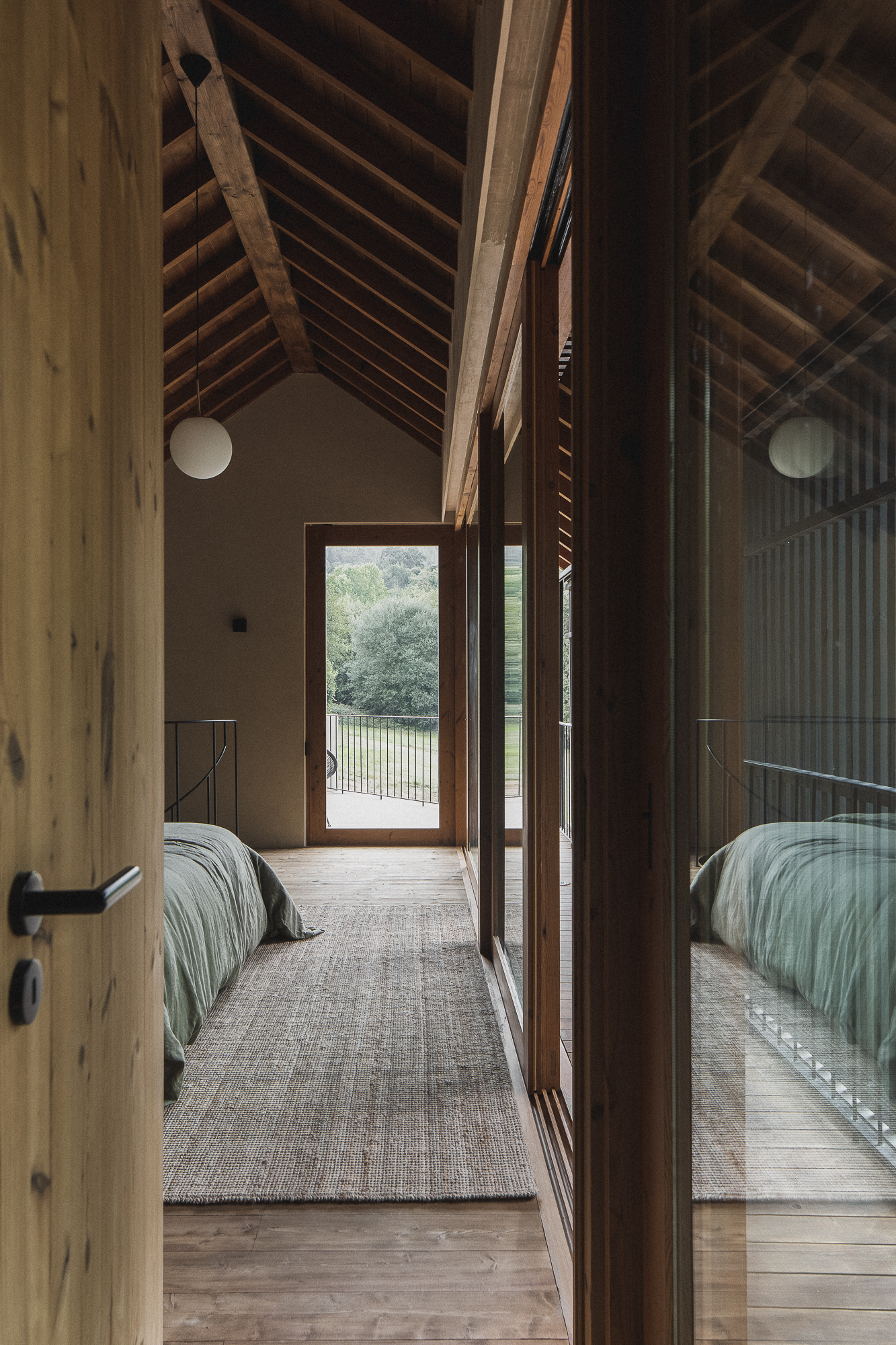 View through doorway into bedroom with exposed timber rafters, glazed wall, and exterior vertical screen beyond