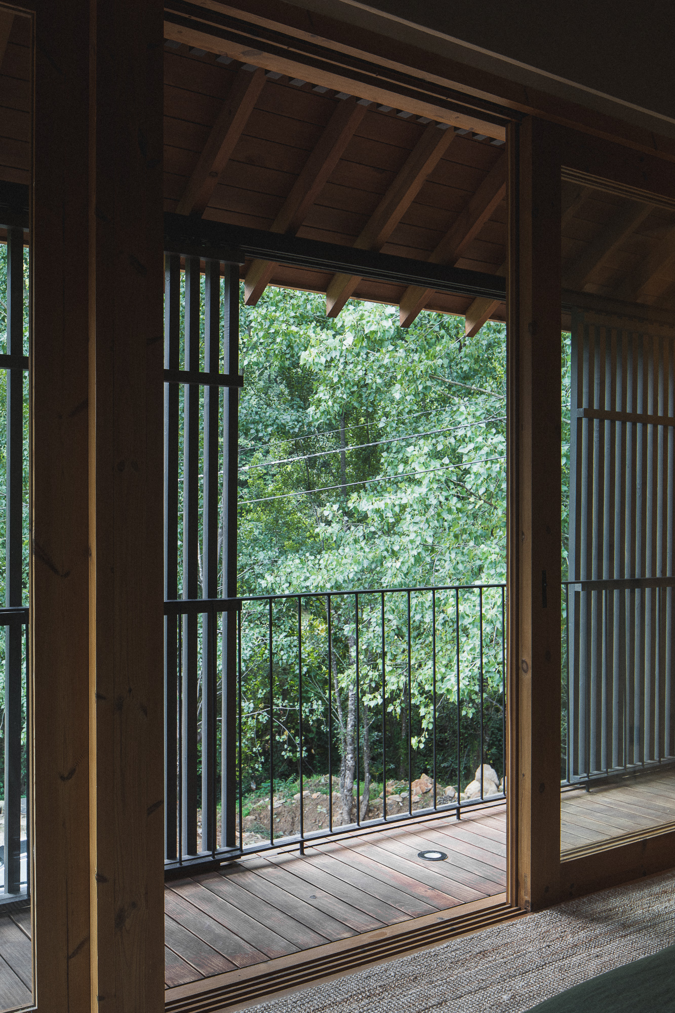 View through open timber doorway to wooden deck with metal railing overlooking green foliage