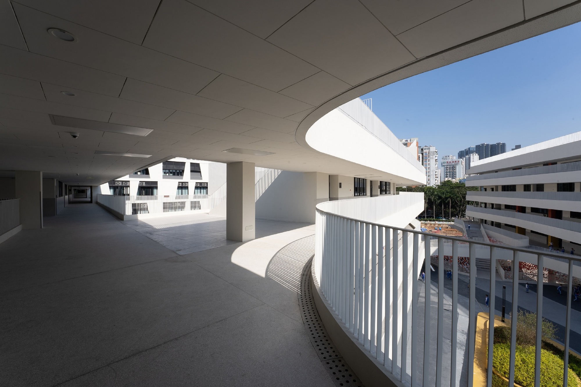 Covered walkway with curved concrete soffit and white vertical balustrade overlooking courtyard buildings