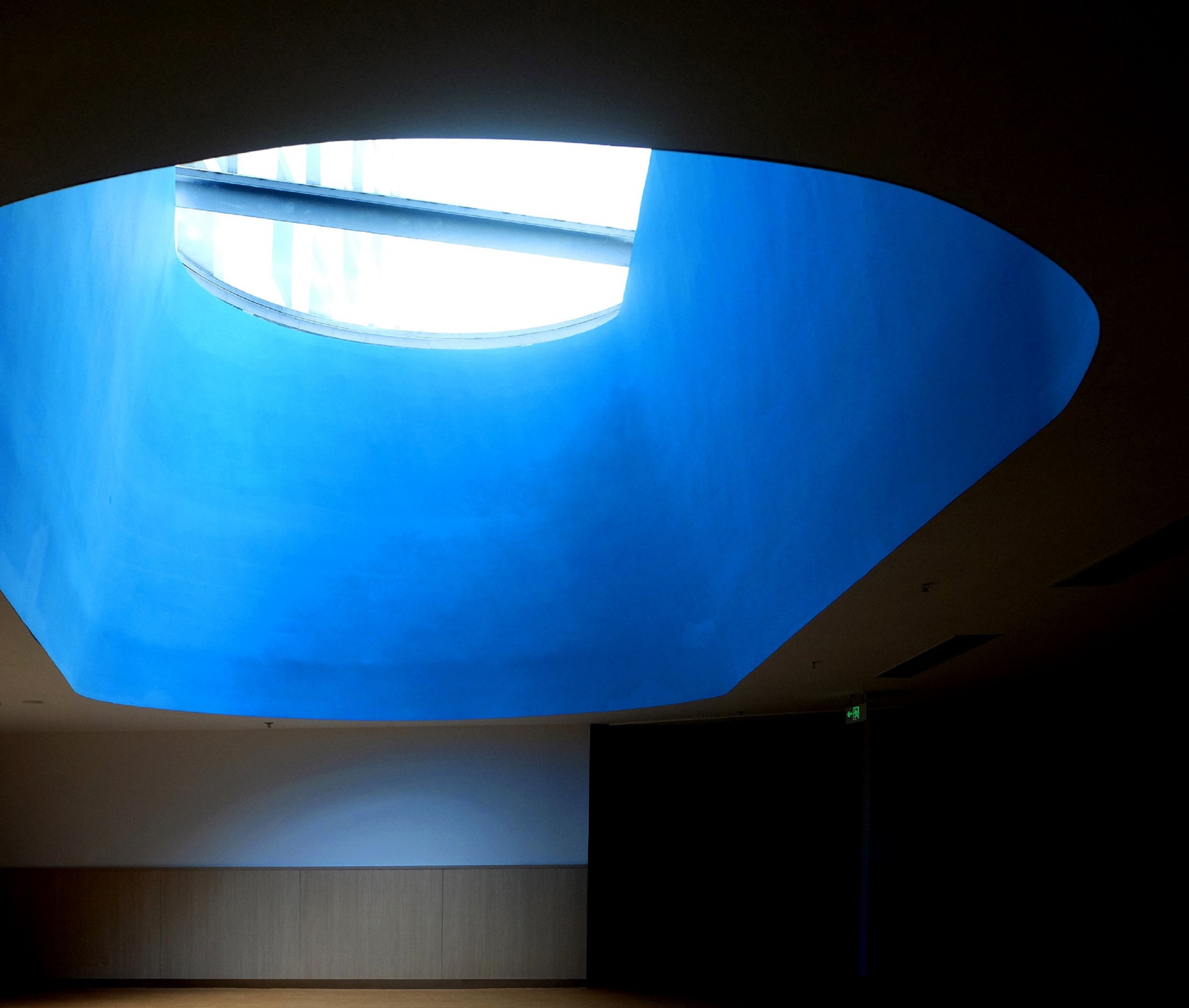 Oval skylight opening with blue sky illuminating the curved interior ceiling from above