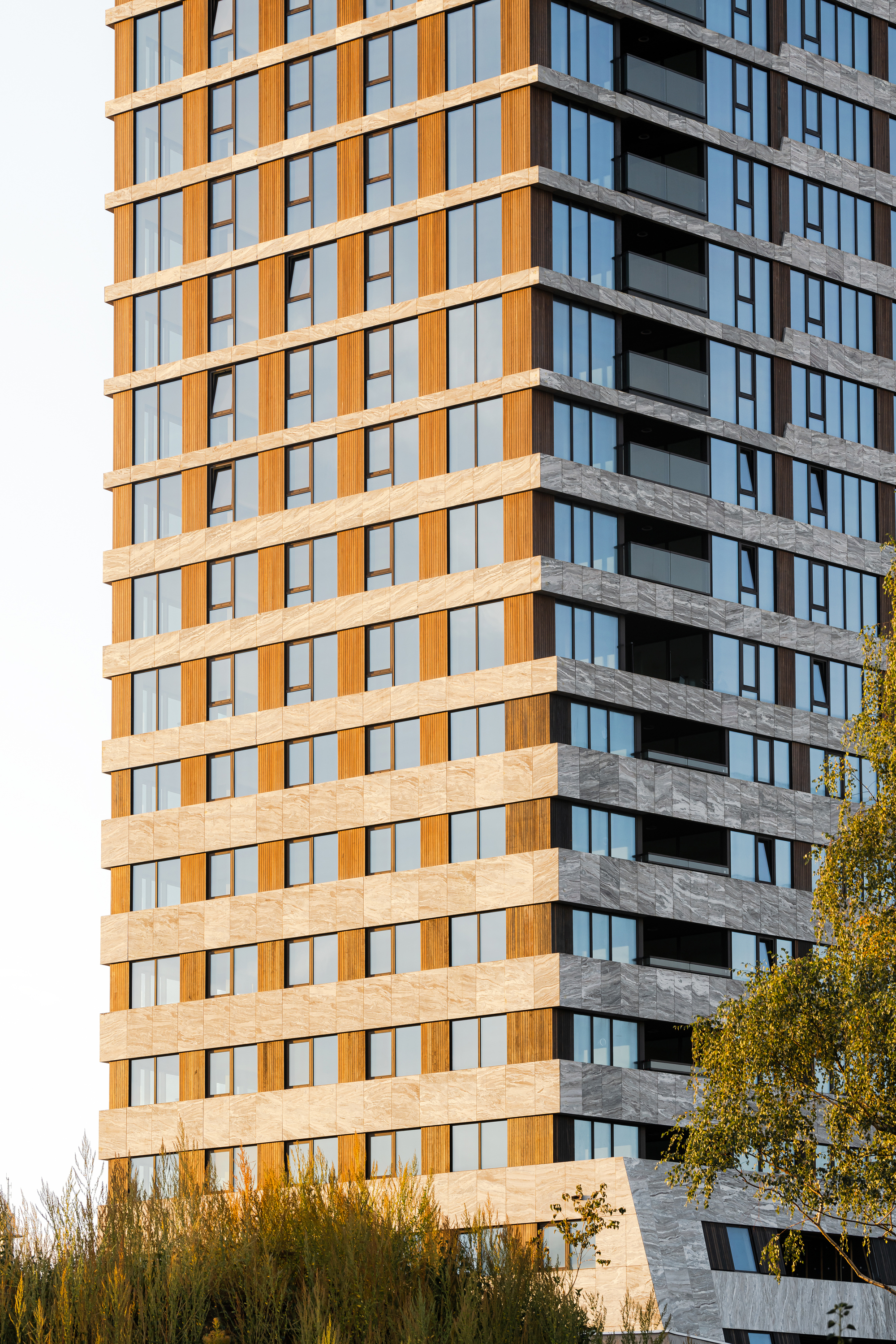 Tower facade with alternating beige and orange panels beside recessed balconies under autumn light