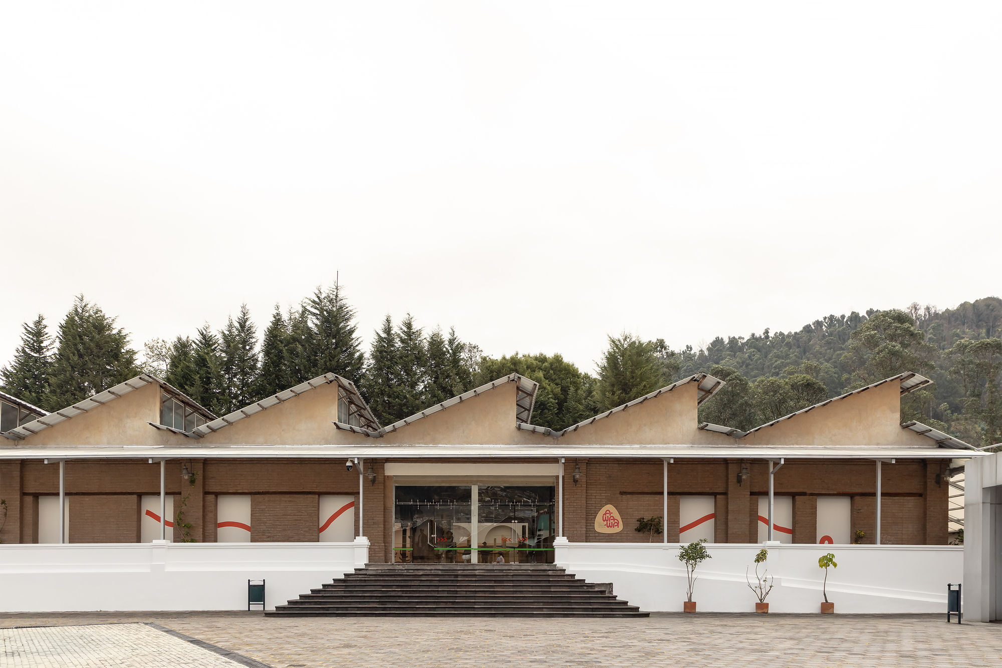 Front facade with repeating sawtooth roofline and central entrance steps leading to a paved plaza