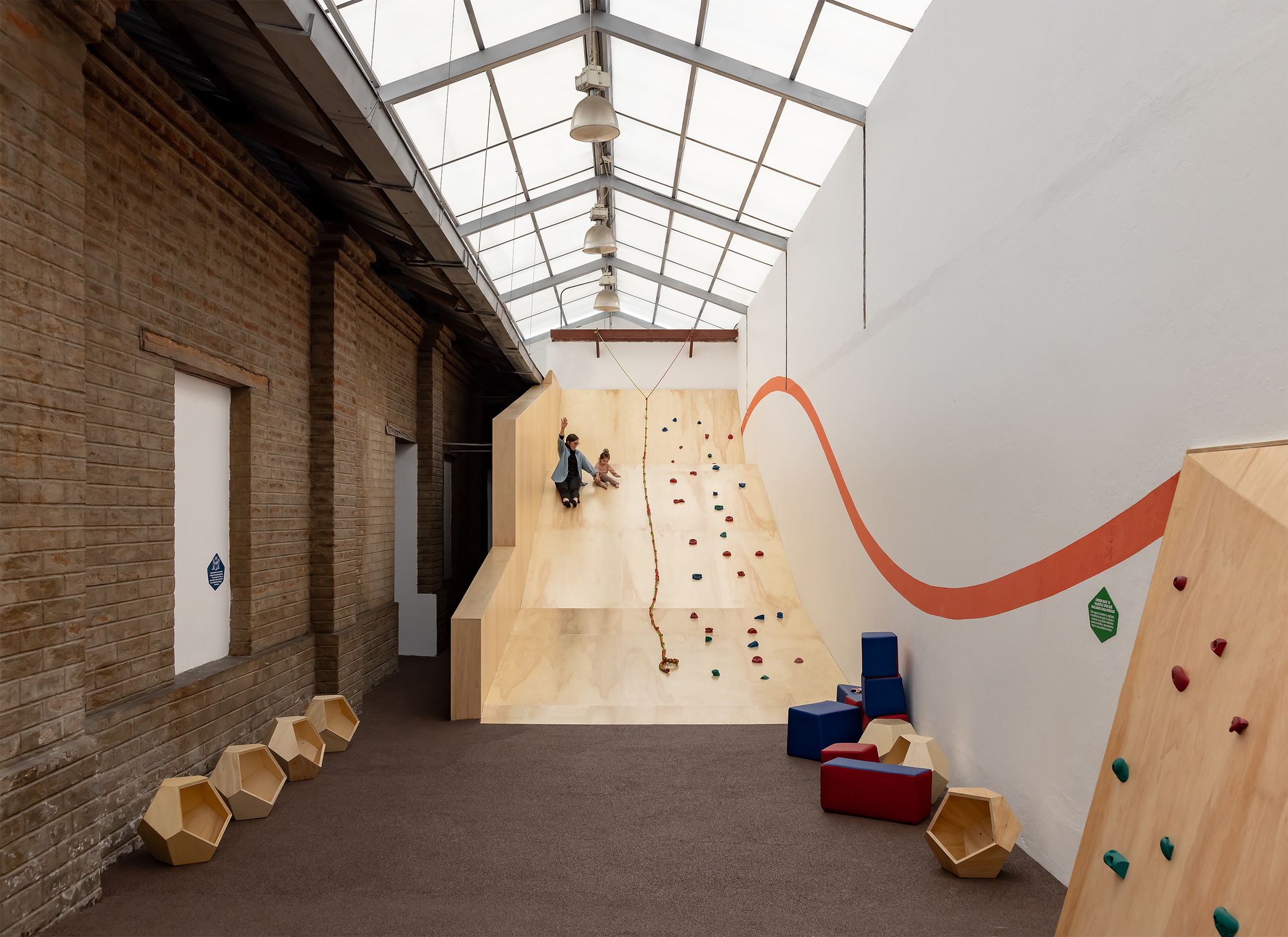 Interior play space with plywood climbing walls and glazed skylight above exposed brick walls