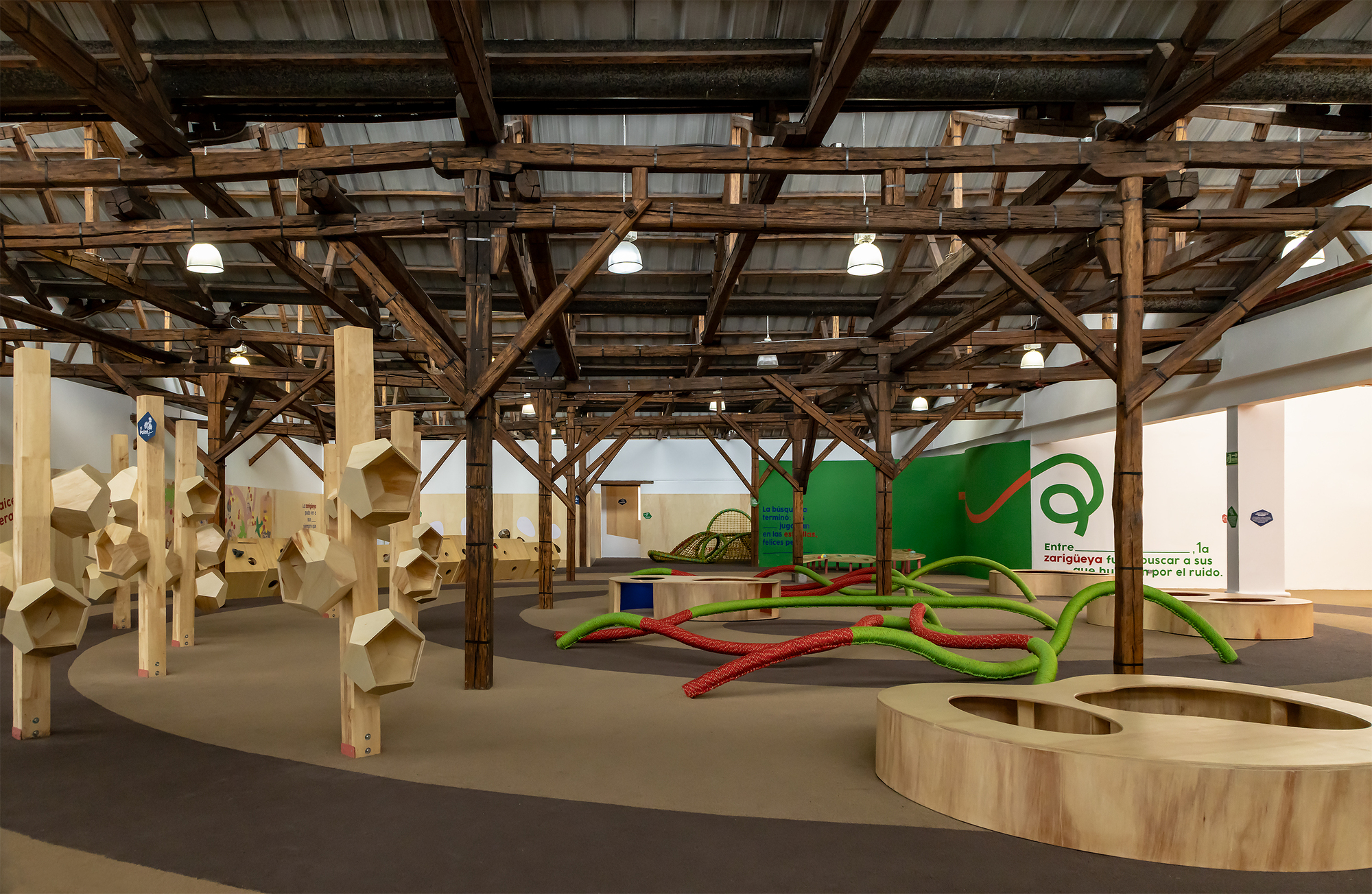Wide view of exhibition space showing timber frame structure with play installations and plywood elements