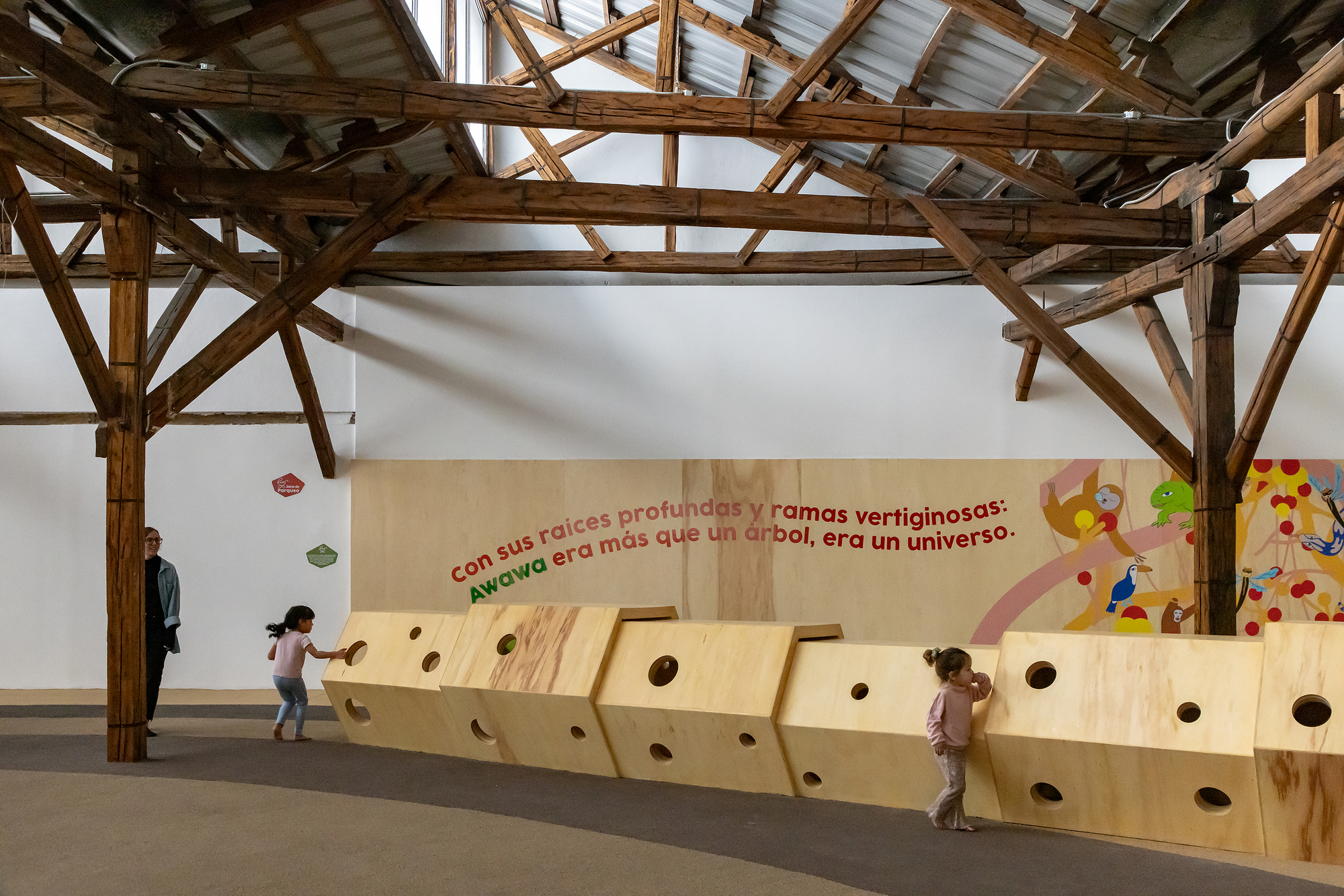 Plywood wall with circular portholes where two children peer through at different heights