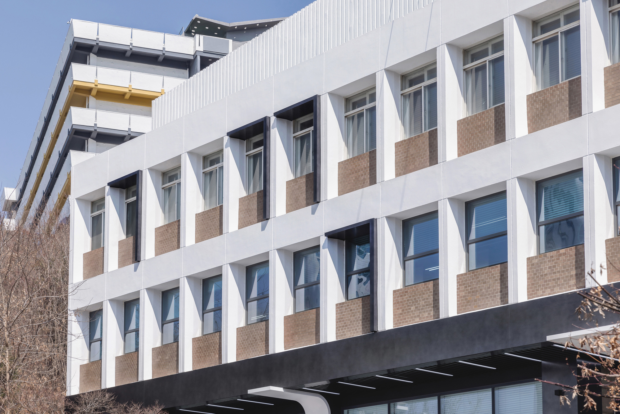 Street facade with zigzag white sunshades alternating with tan brick panels under a clear sky