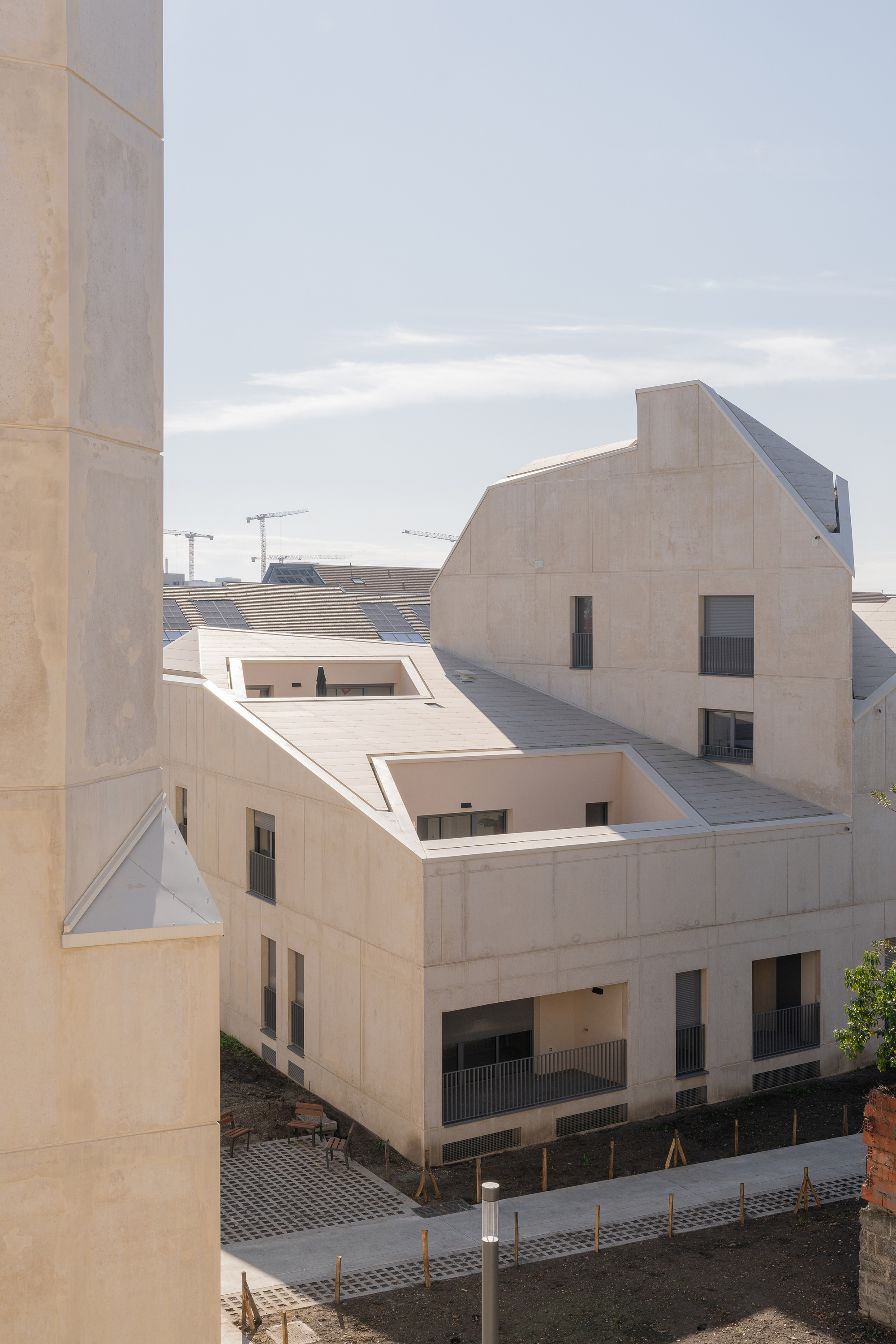 Pale concrete facade with staggered roofline and punched window openings under an overcast sky