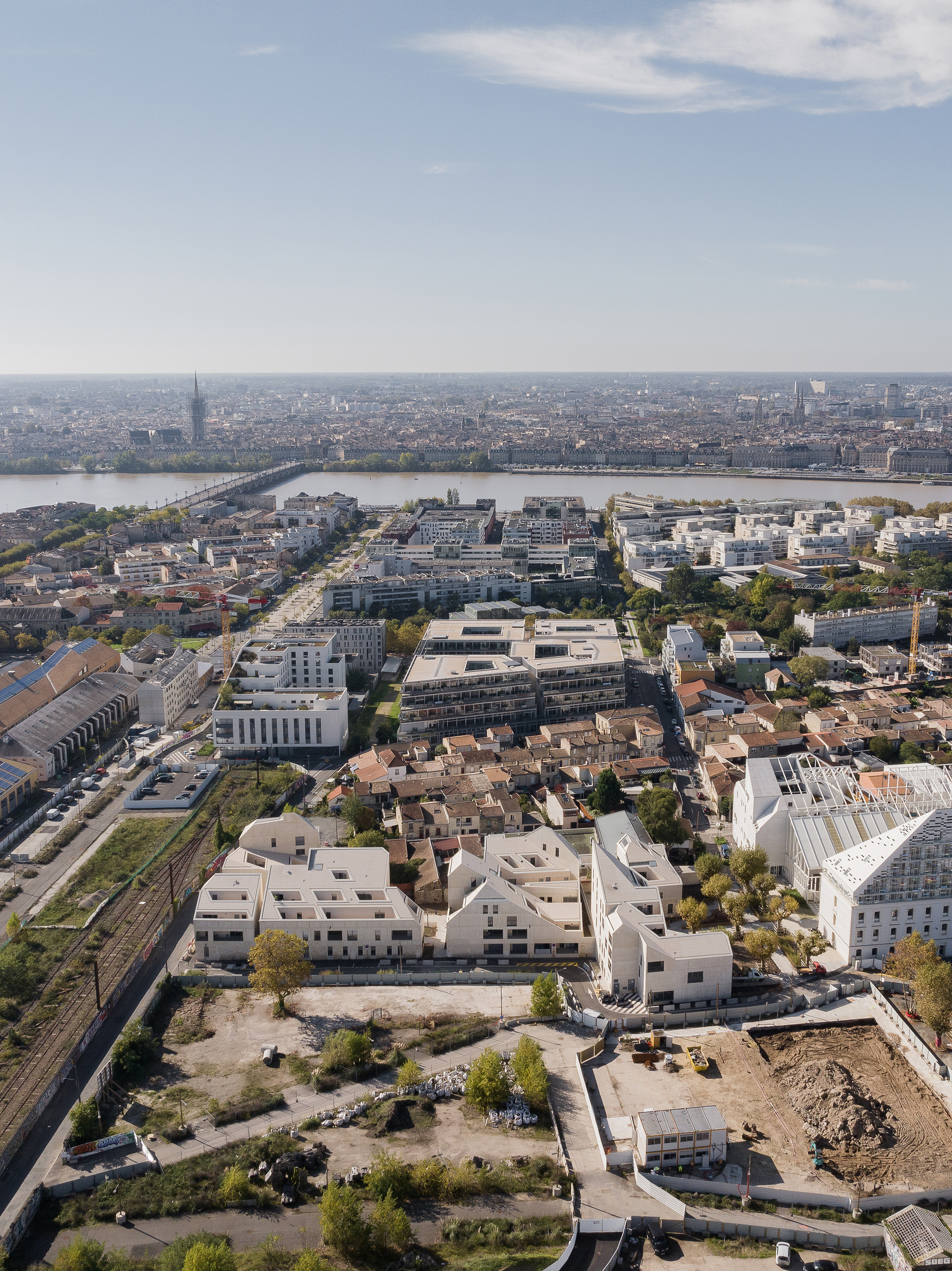 Aerial overview of the low-rise housing complex among railway lines with a river and distant skyline