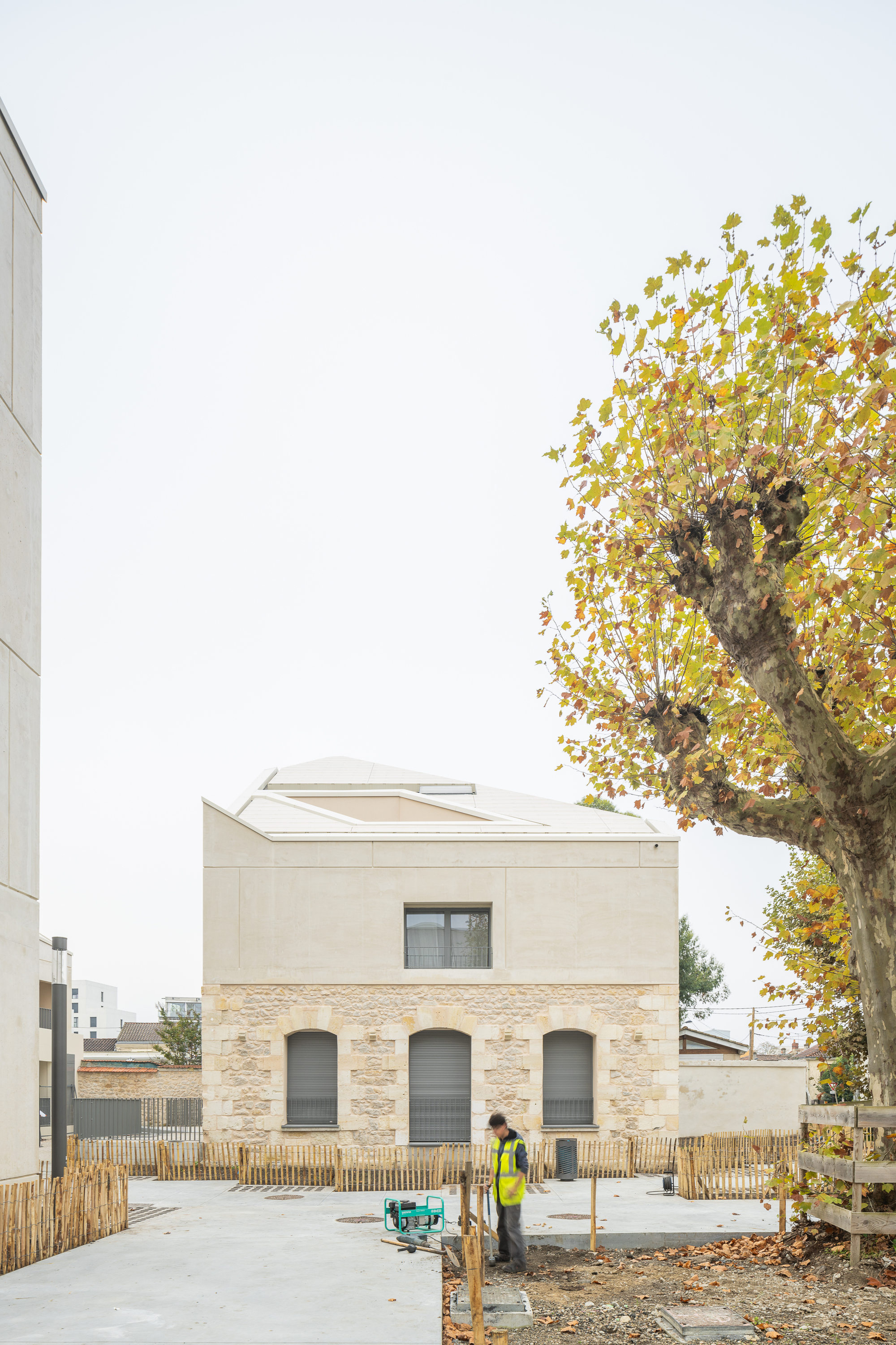 Street view of the stone base and rendered upper floor with a worker and autumn tree in front