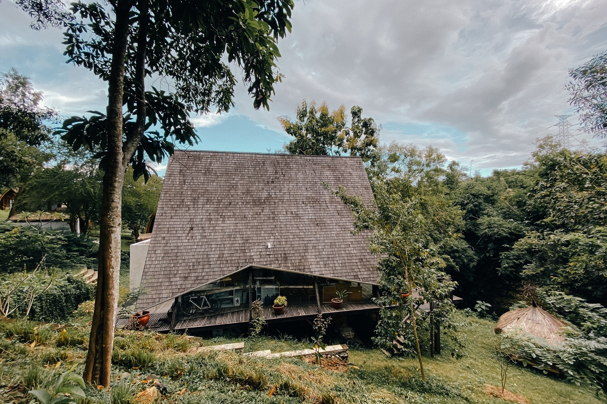 A-frame structure with grey tile roof and timber balcony nestled among dense vegetation