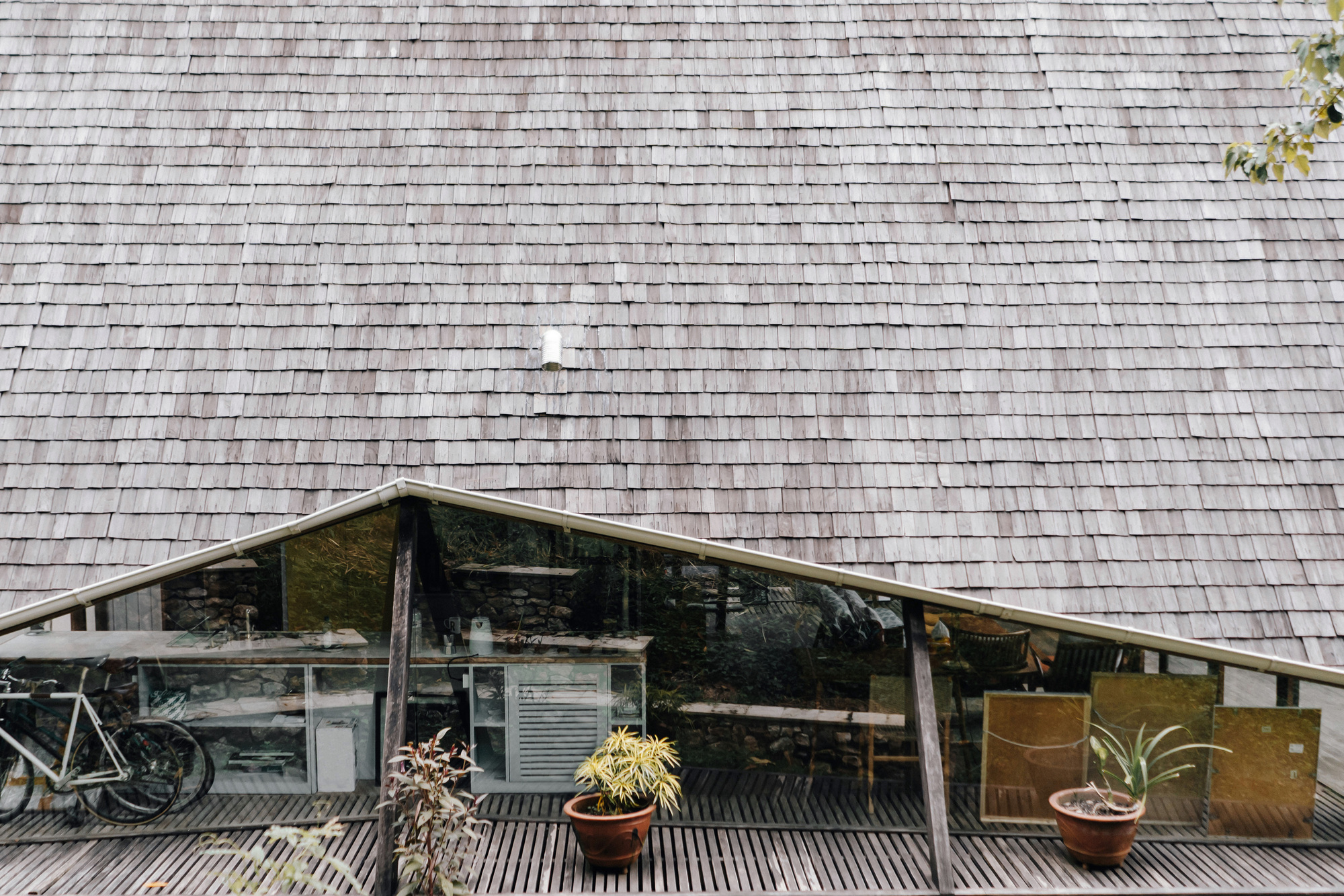 Weathered wooden shingle roof above a recessed terrace with horizontal slat flooring and potted plants