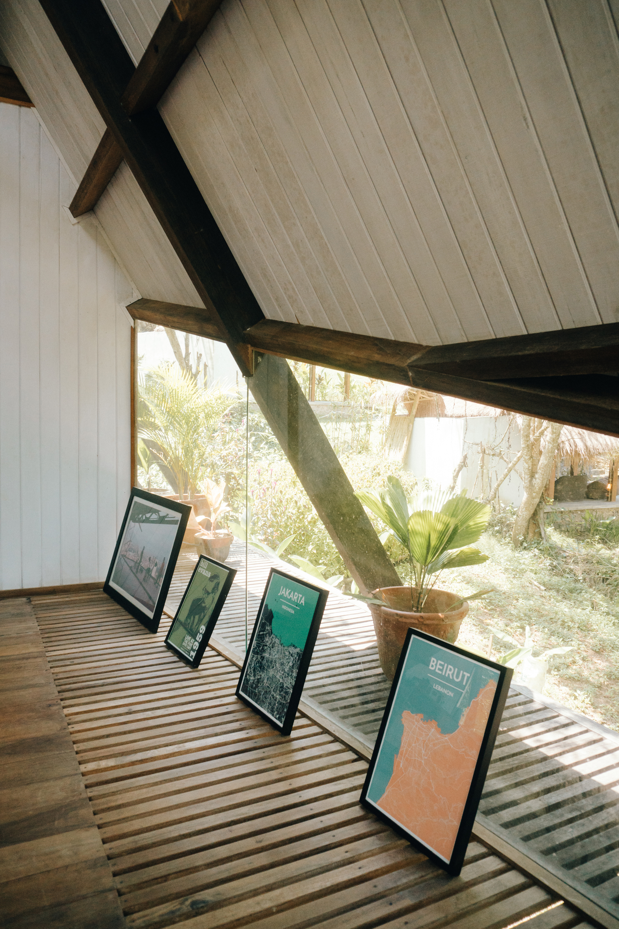 Slatted timber floor supporting a row of framed posters and a potted plant beneath angled beams