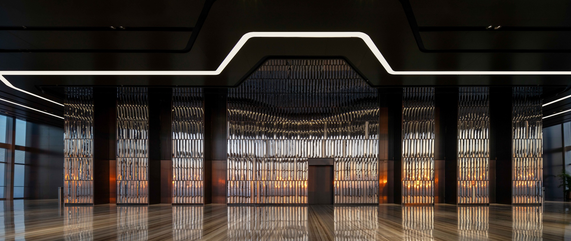 Symmetrical view of backlit metal screen panels between dark columns under geometric ceiling cutout