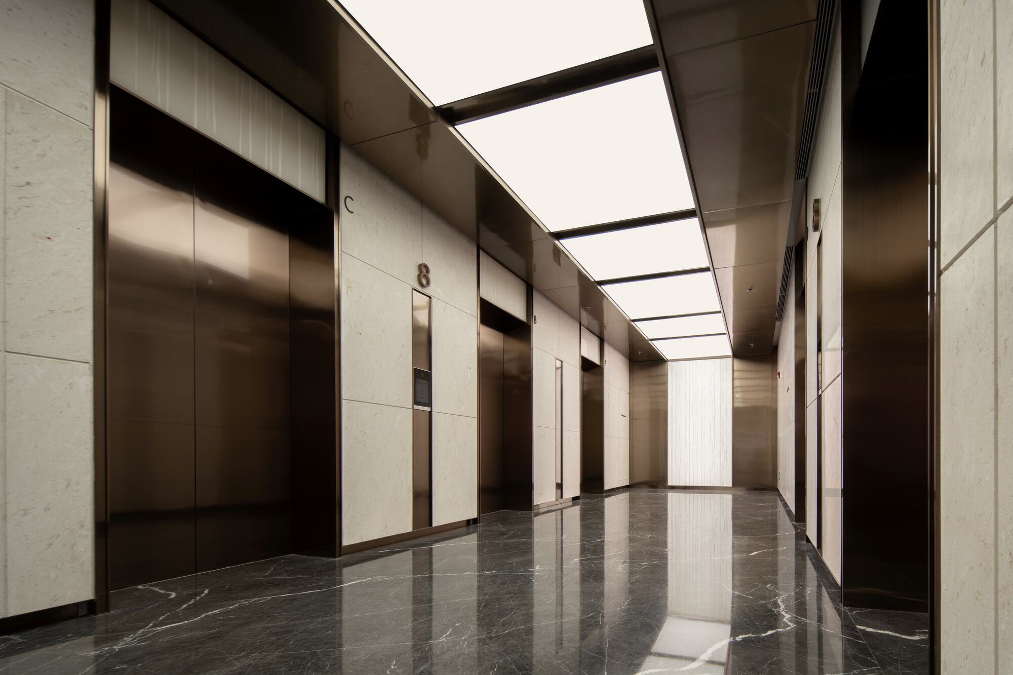 Elevator lobby with bronze-framed doors and backlit ceiling panels over dark veined marble floor