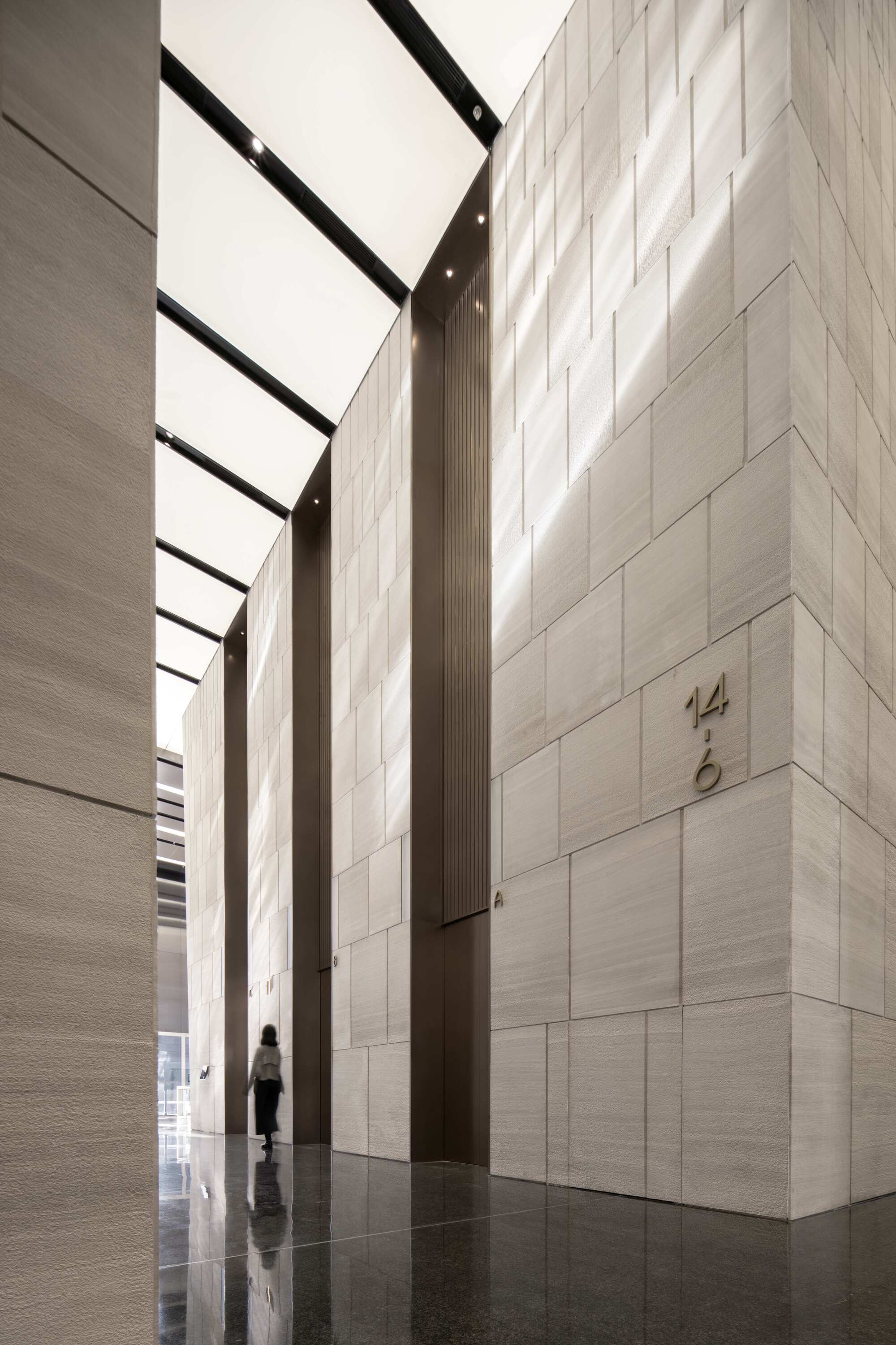 Tall lobby with pale stone block walls and a skylight casting natural light onto a polished floor