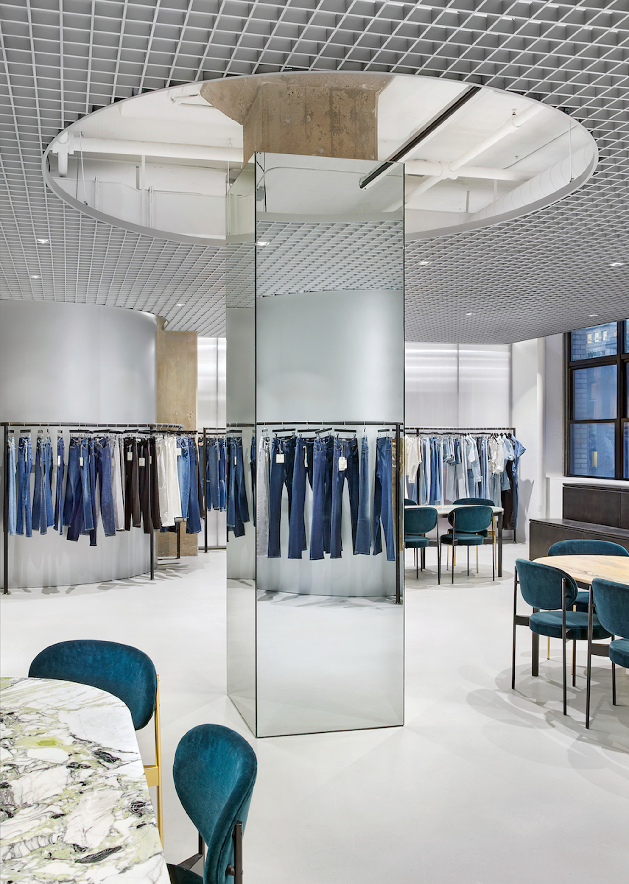 Circular ceiling oculus above mirrored column clad in polished metal panels reflecting the showroom floor
